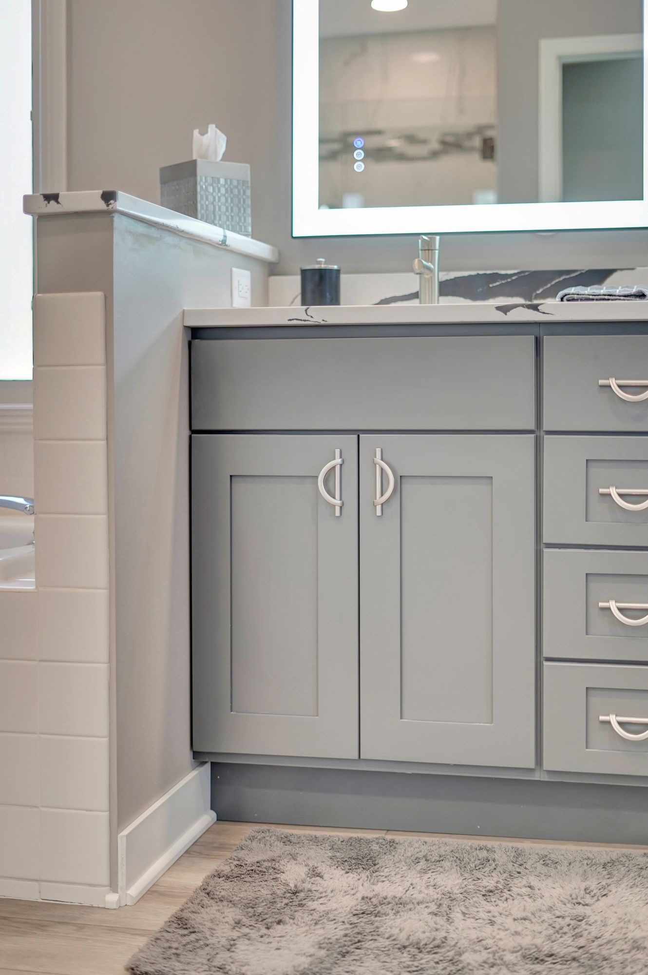 Gray bathroom vanity with silver hardware and a lit mirror.