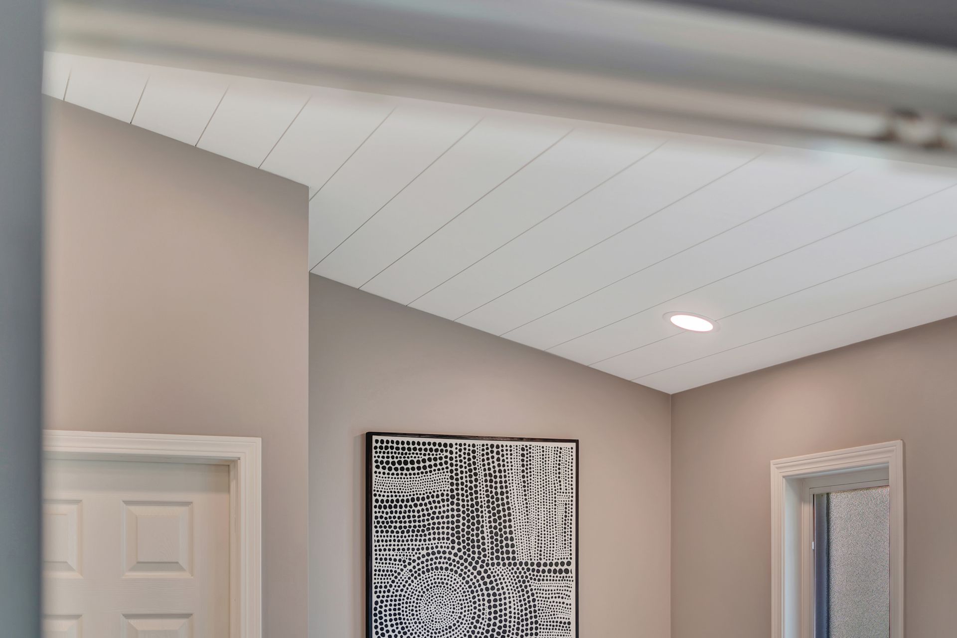 Room with angled ceiling, light walls, recessed lighting, white panel ceiling, artwork, and two doorways.