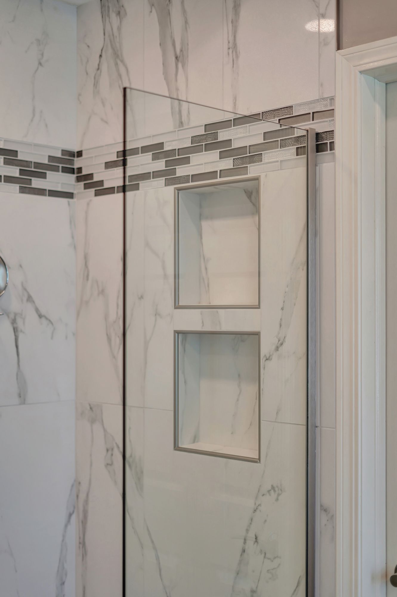 White marble tile shower with glass doors, built-in shelf, and decorative tile border.