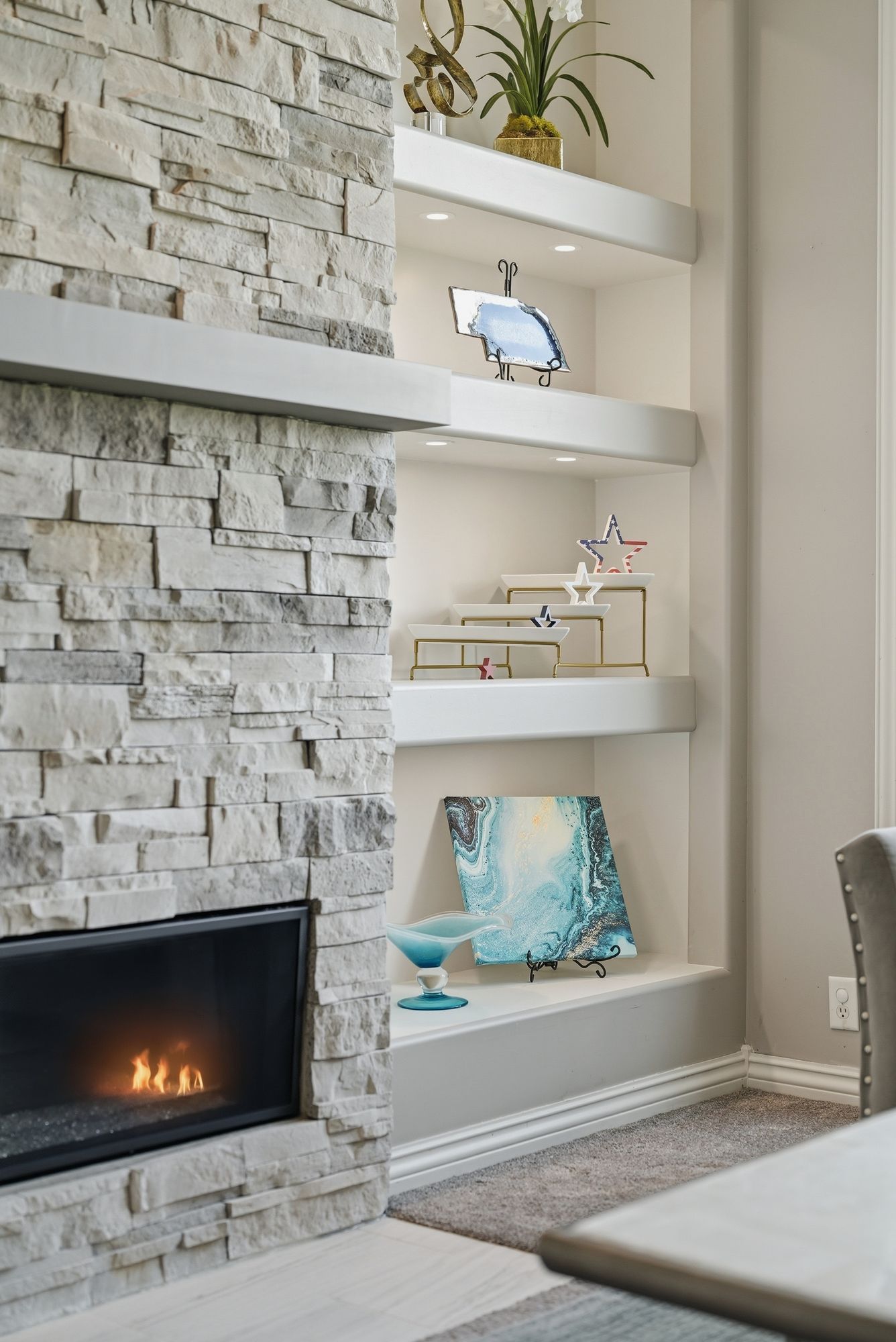 Modern living room corner with white shelves, stacked stone fireplace, and blue decorative accents