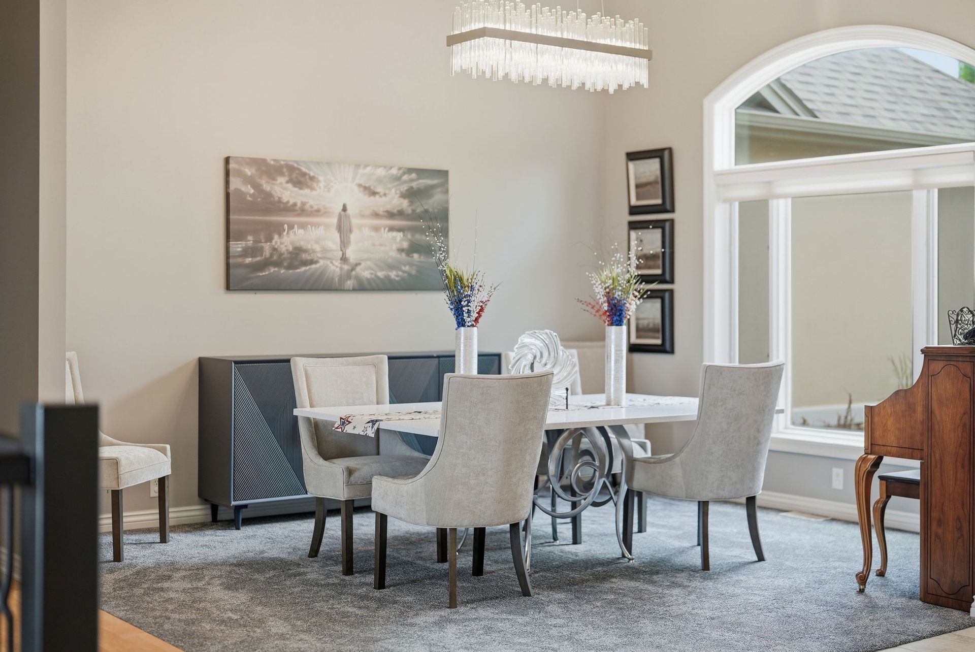 Bright dining room with white table, upholstered chairs, floral centerpiece, and large wall art