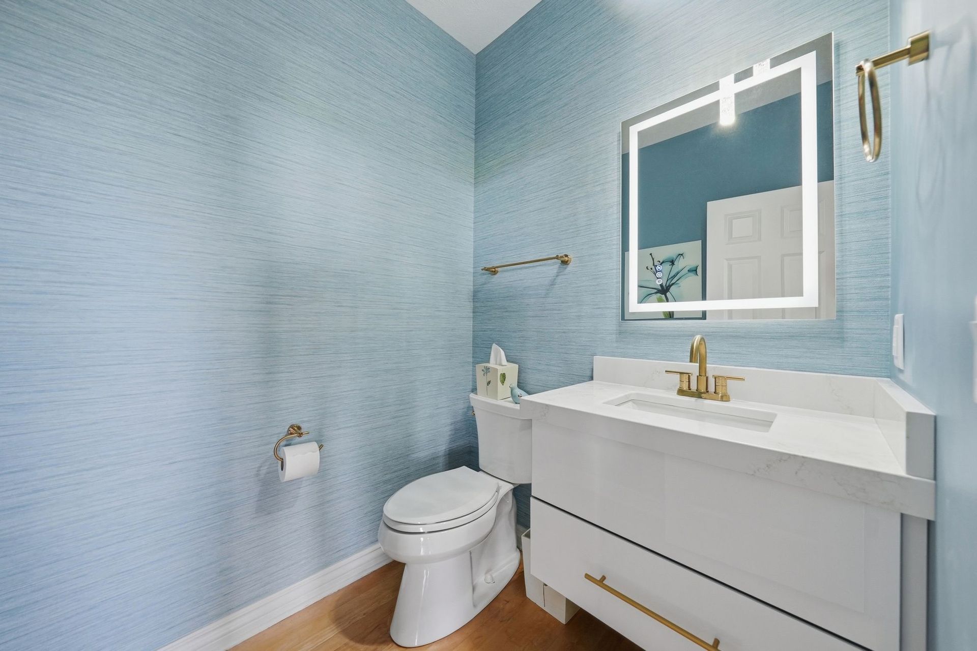 Light blue bathroom with white vanity, mirror, toilet, and gold fixtures