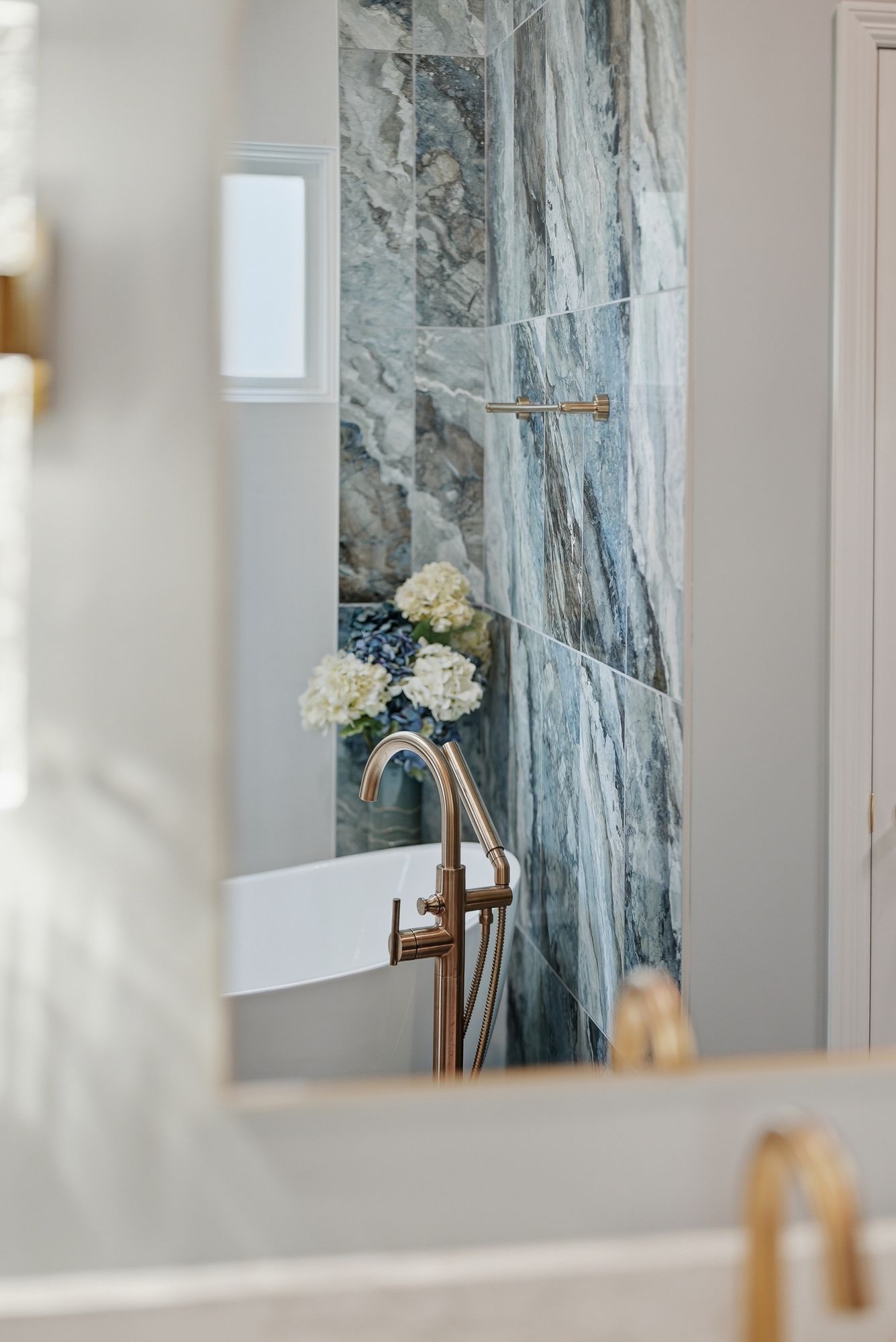 Modern bathroom with a marble-tiled shower, brass fixtures, and a white flower arrangement in a vase