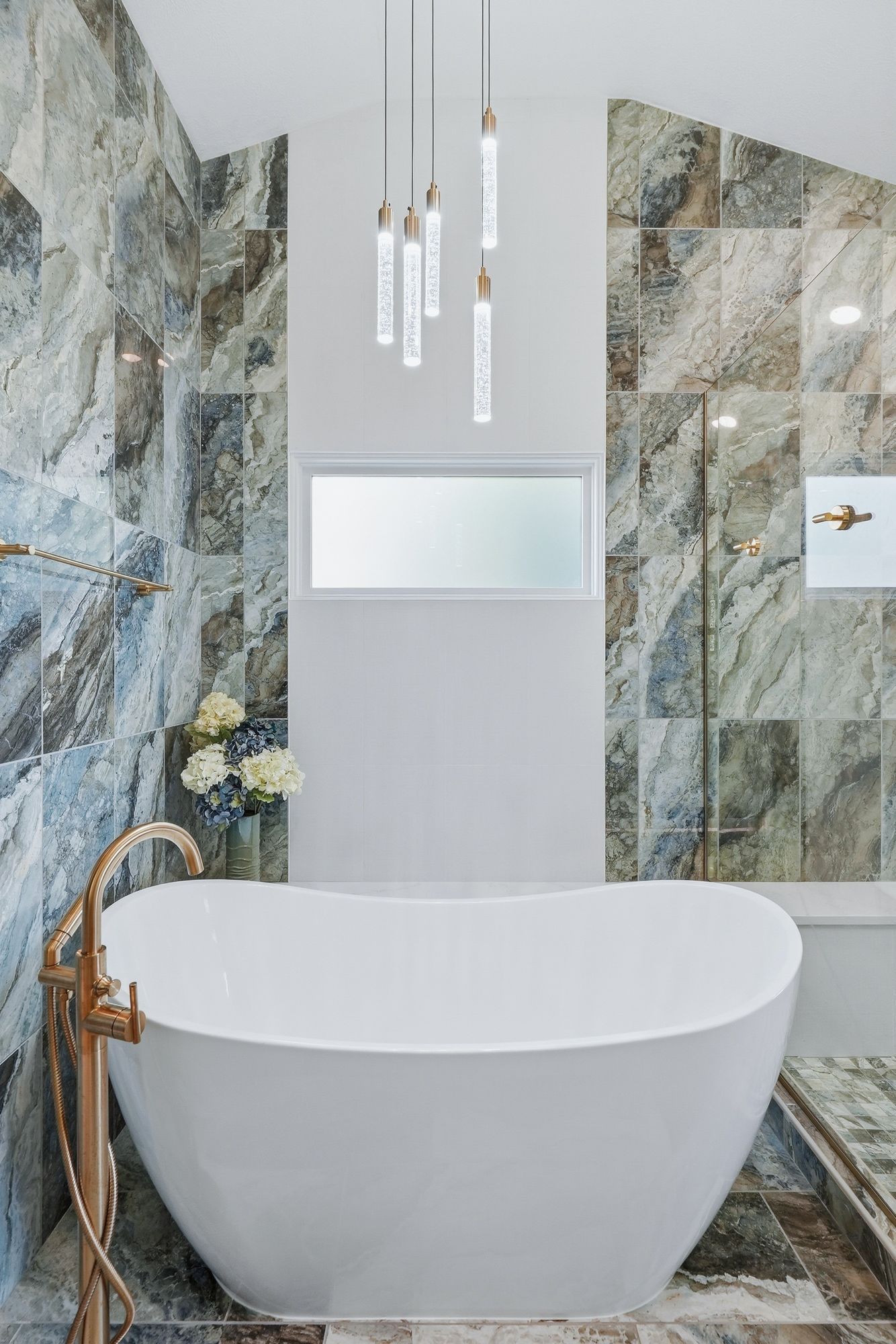 Modern bathroom with a white freestanding tub, marble walls, and pendant lights