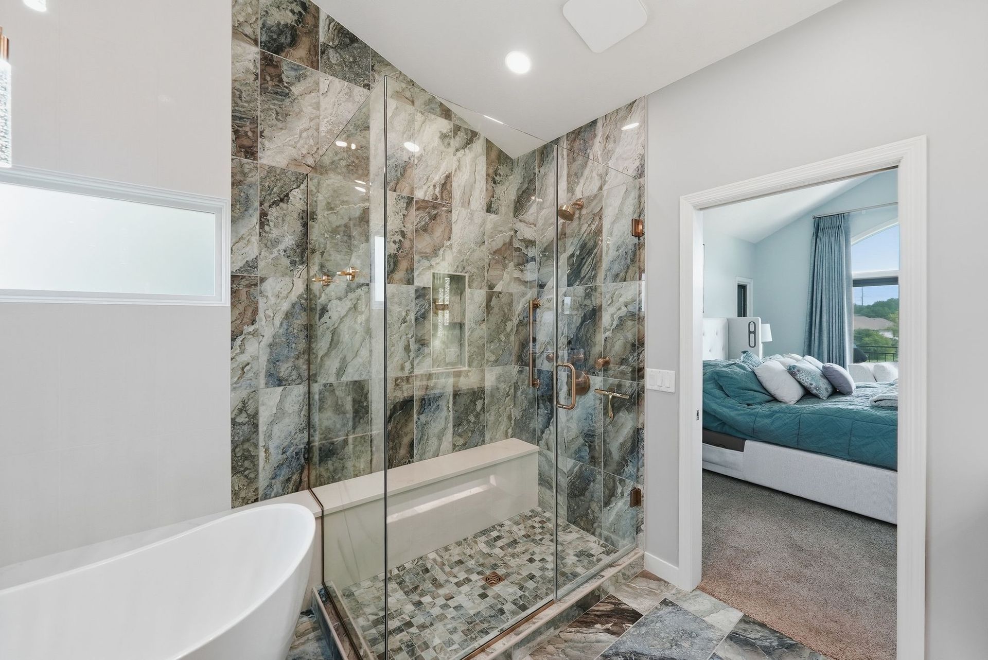 Modern bathroom with marble-patterned shower and tiled floor, open doorway to a bedroom with teal bedding