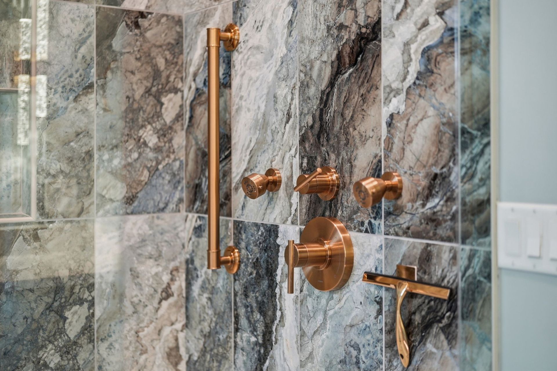 Bronze shower fixtures on a gray marble-tile glass shower wall