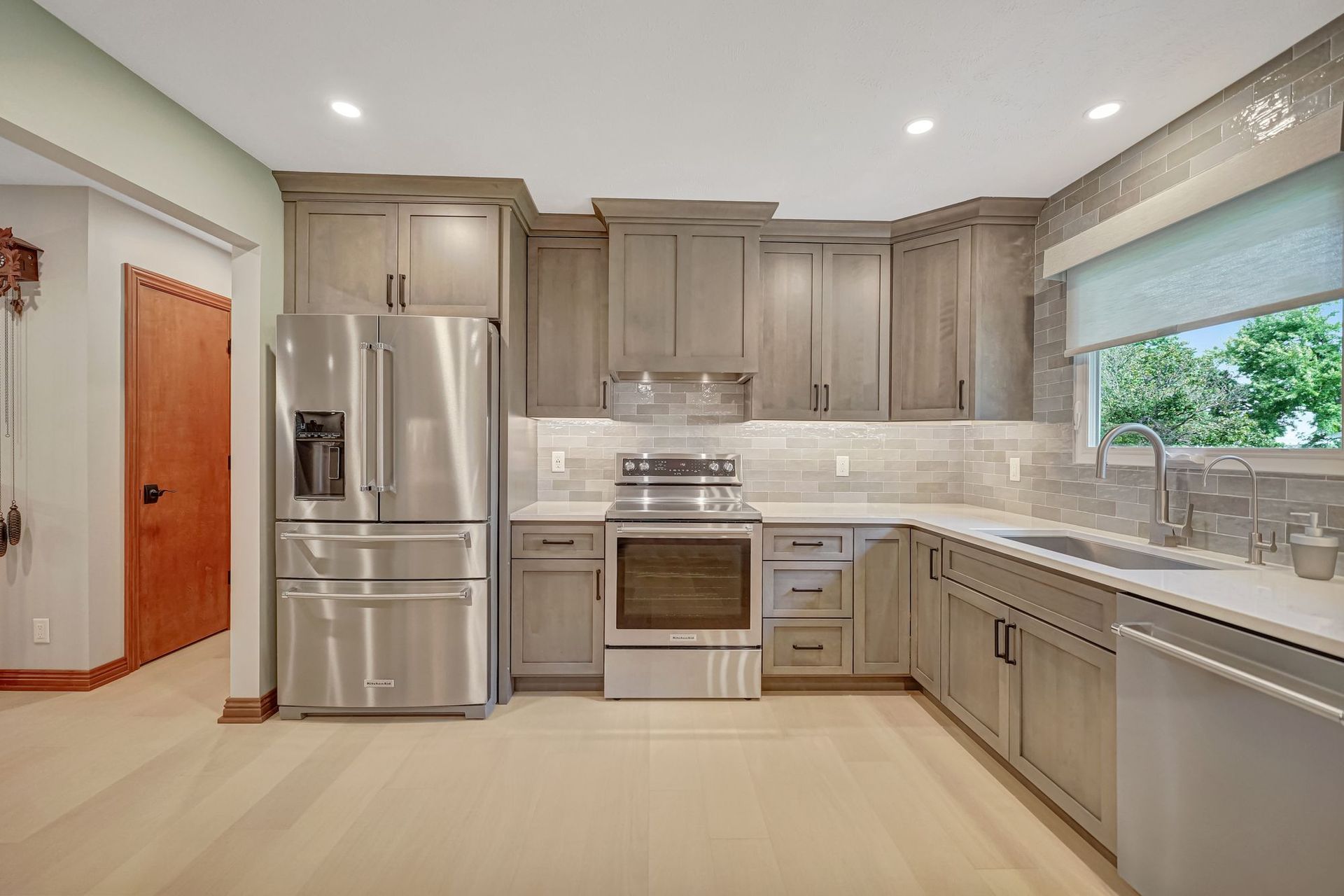 Gray-toned kitchen with stainless steel appliances, light countertops, and a window.