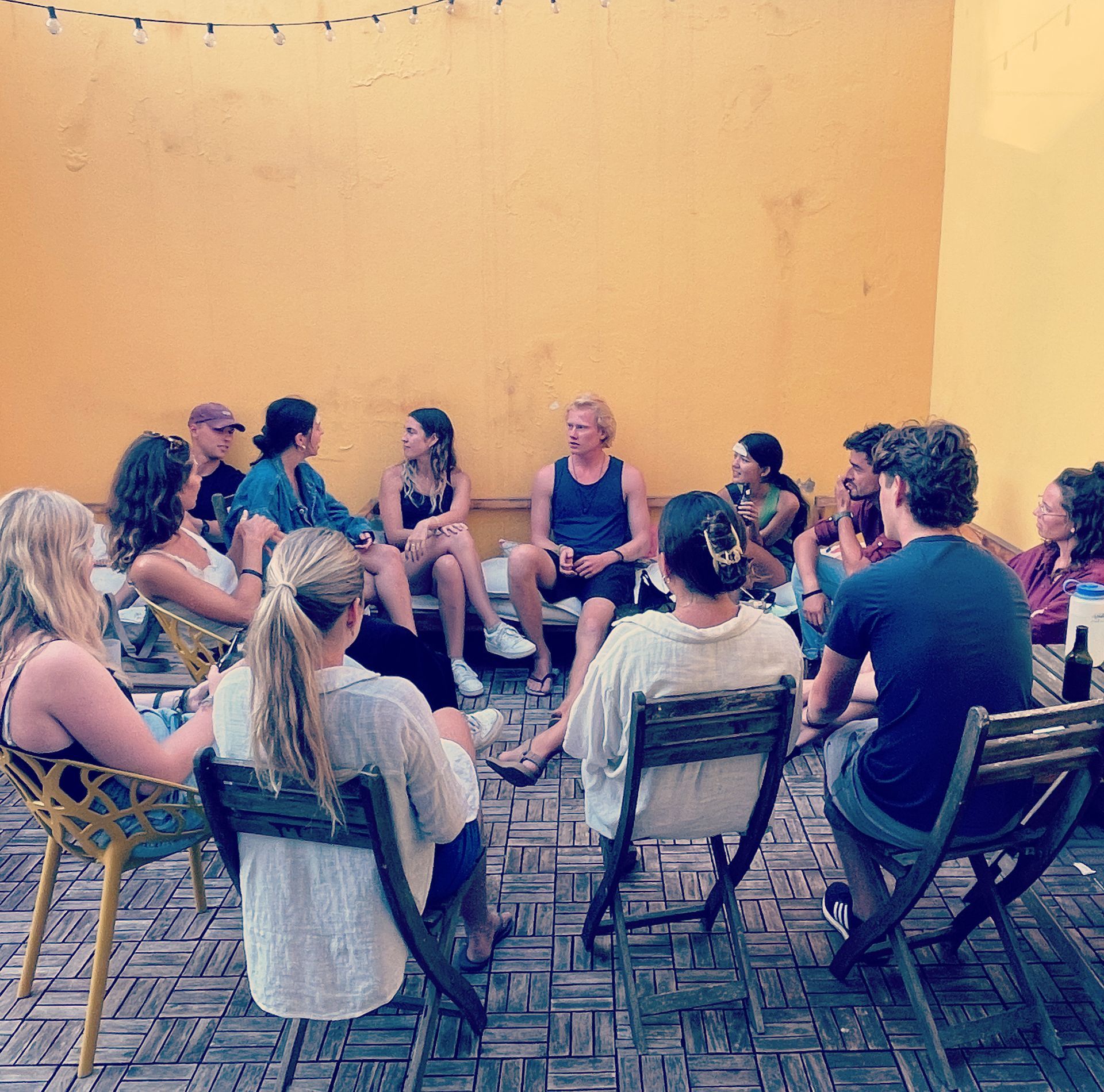 A group of people are sitting in a circle in front of a yellow wall