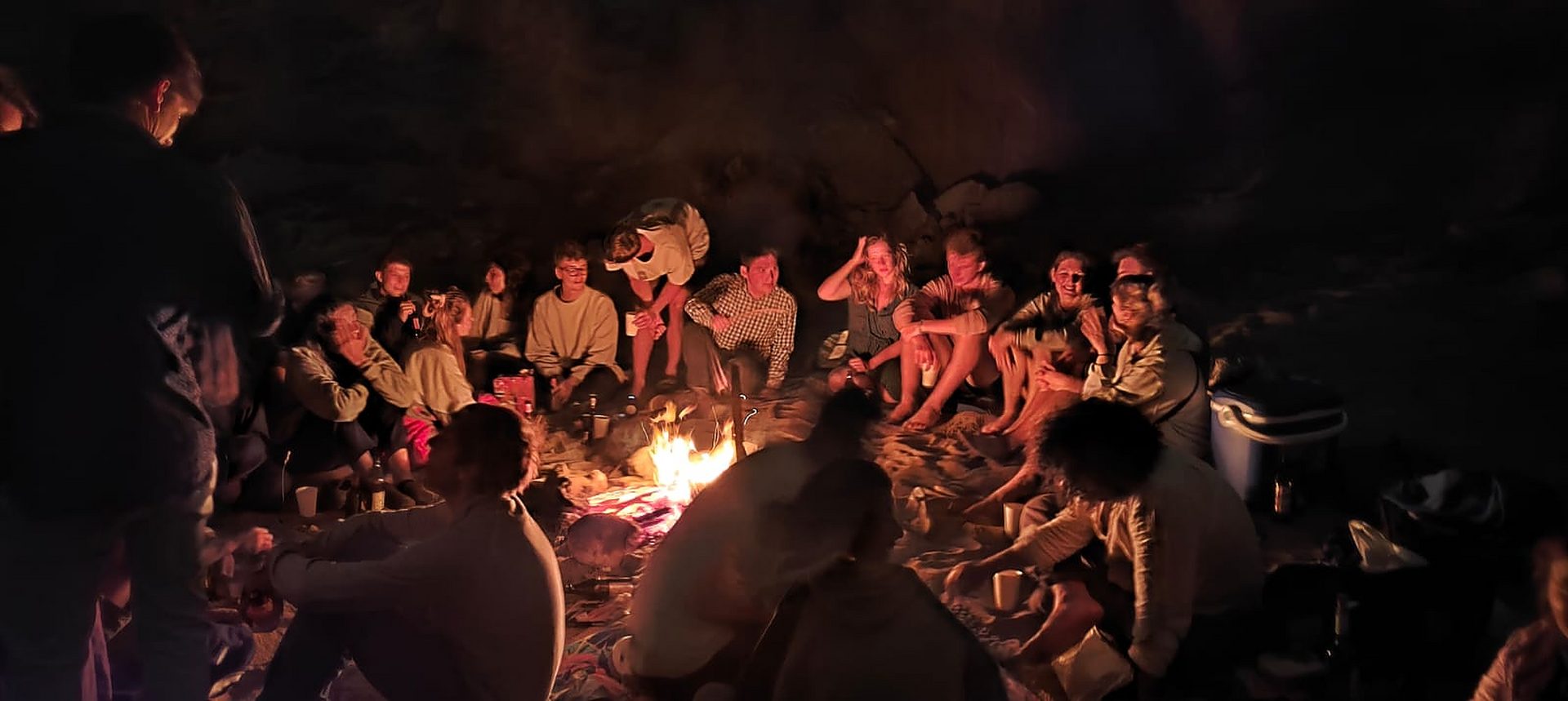 A group of people are gathered around a campfire at night.