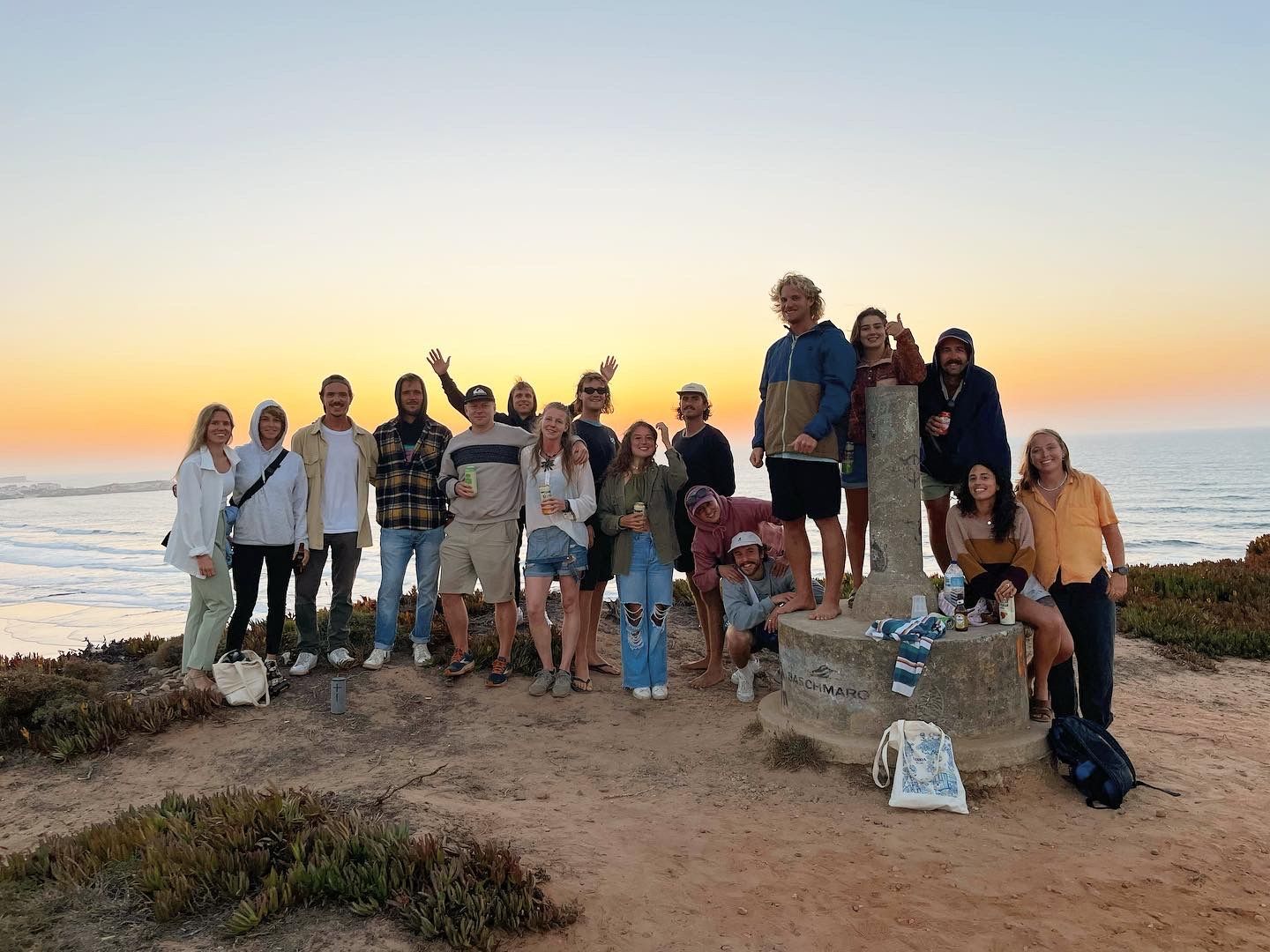 A group of people are posing for a picture on a beach at sunset.
