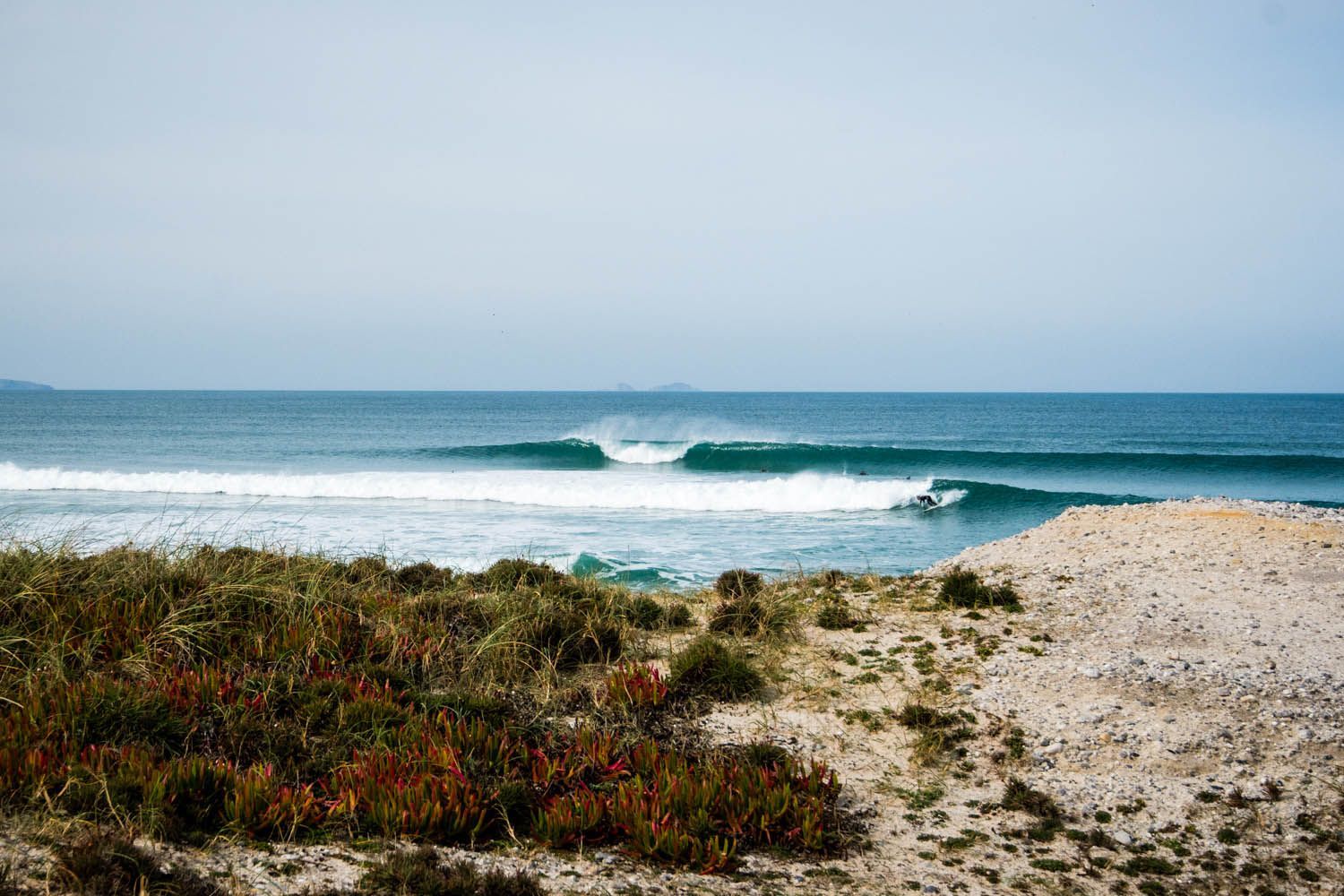 A surfer is riding a wave in the ocean on a sandy beach.