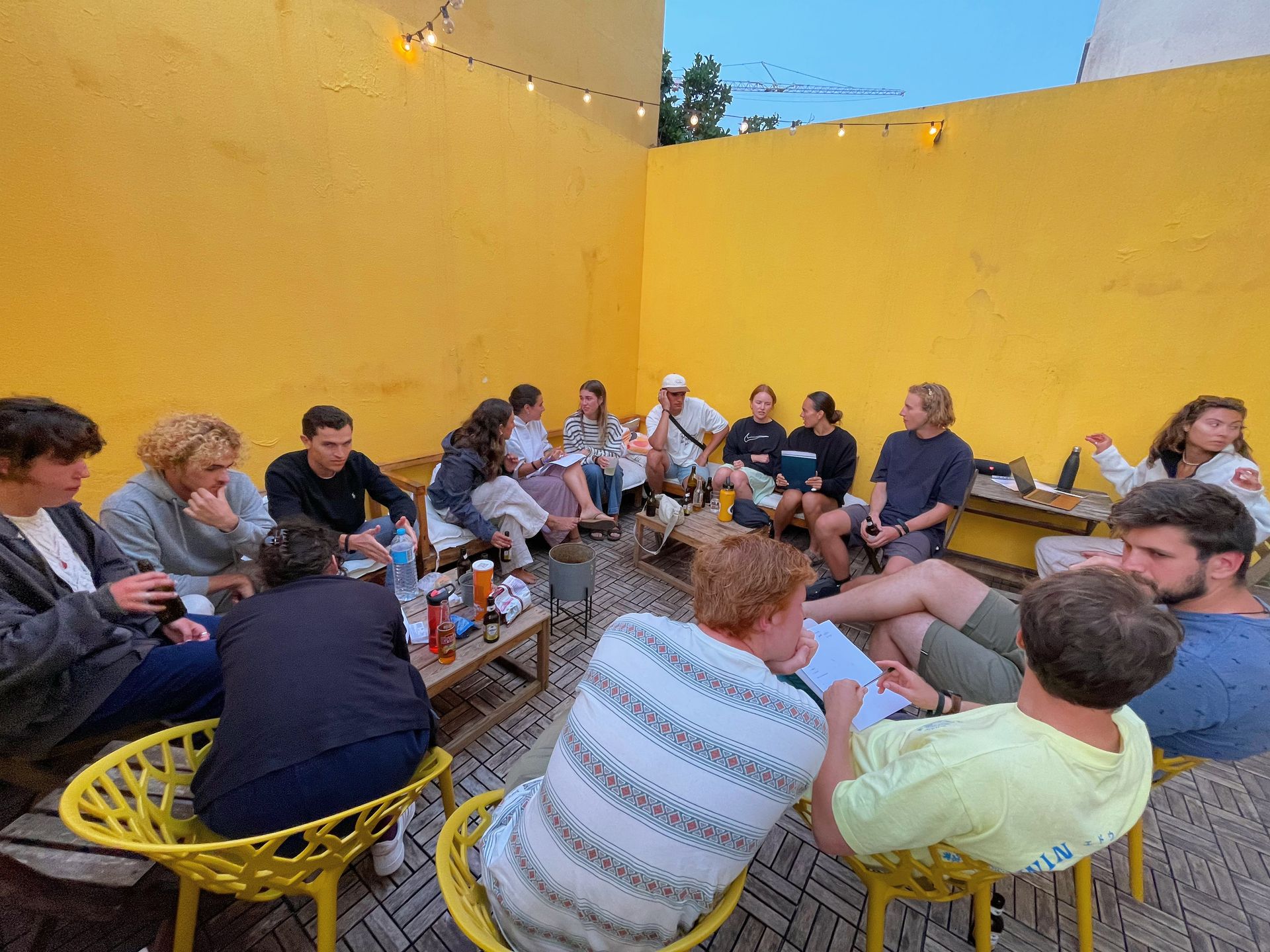 A group of people are sitting in a circle in front of a yellow wall.