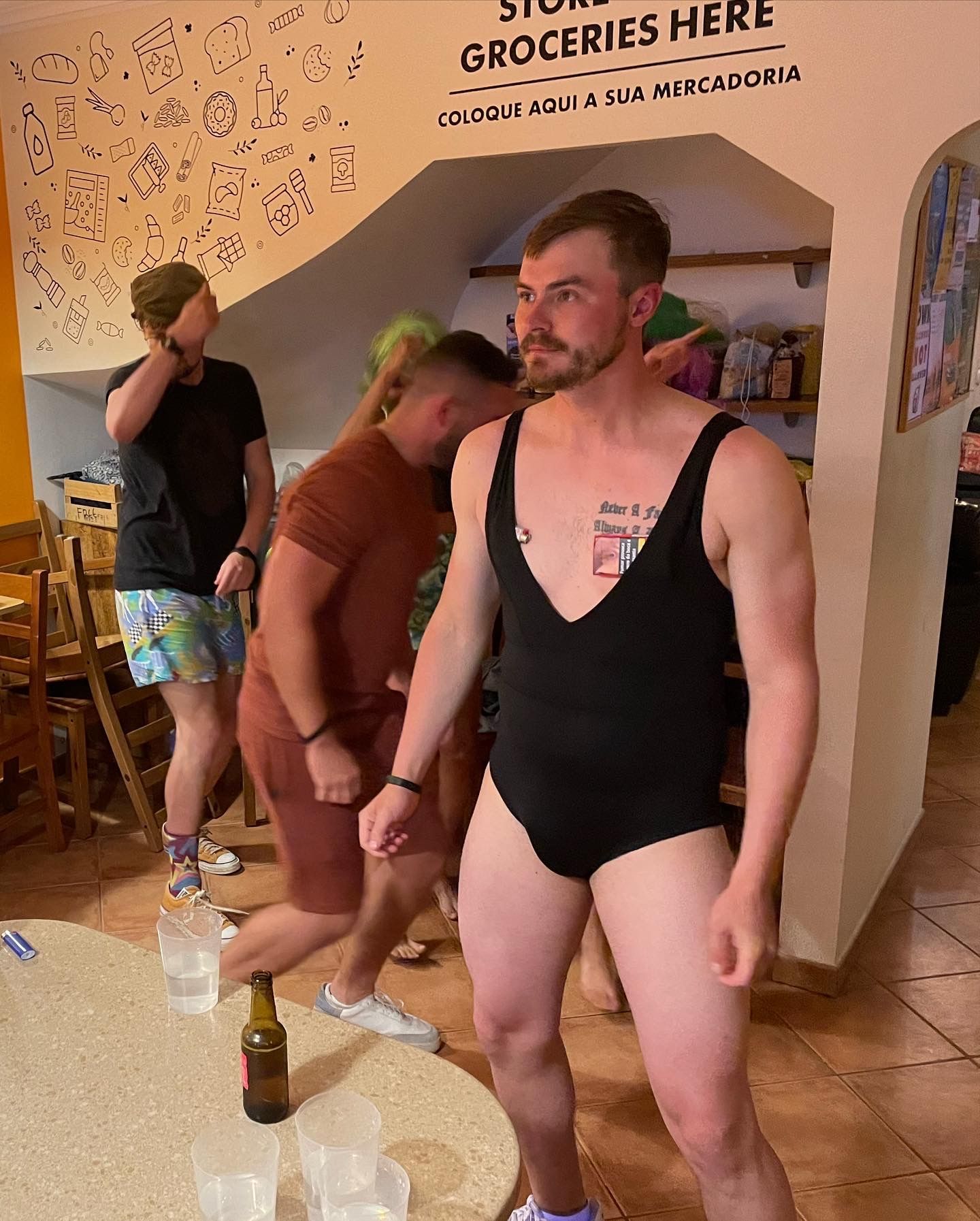 A man in a swimsuit is standing in front of a sign that says groceries here