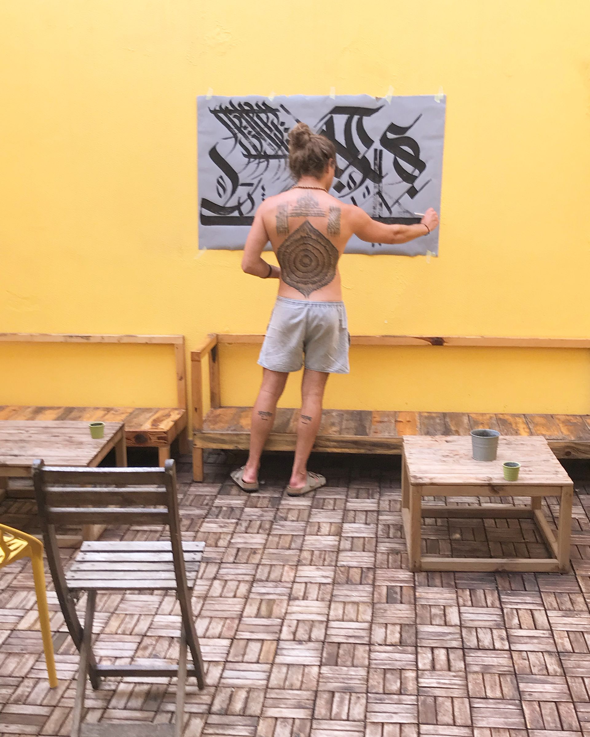 A woman with a tattoo on her back is standing in front of a yellow wall.