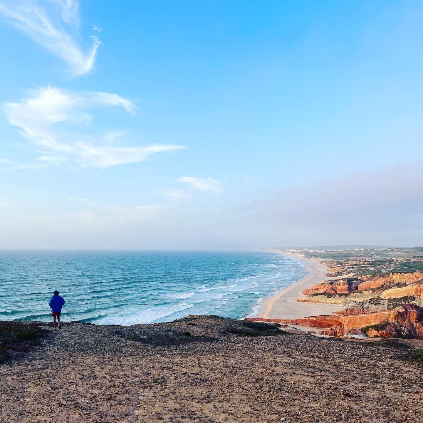 A man is standing on top of a hill overlooking the ocean.