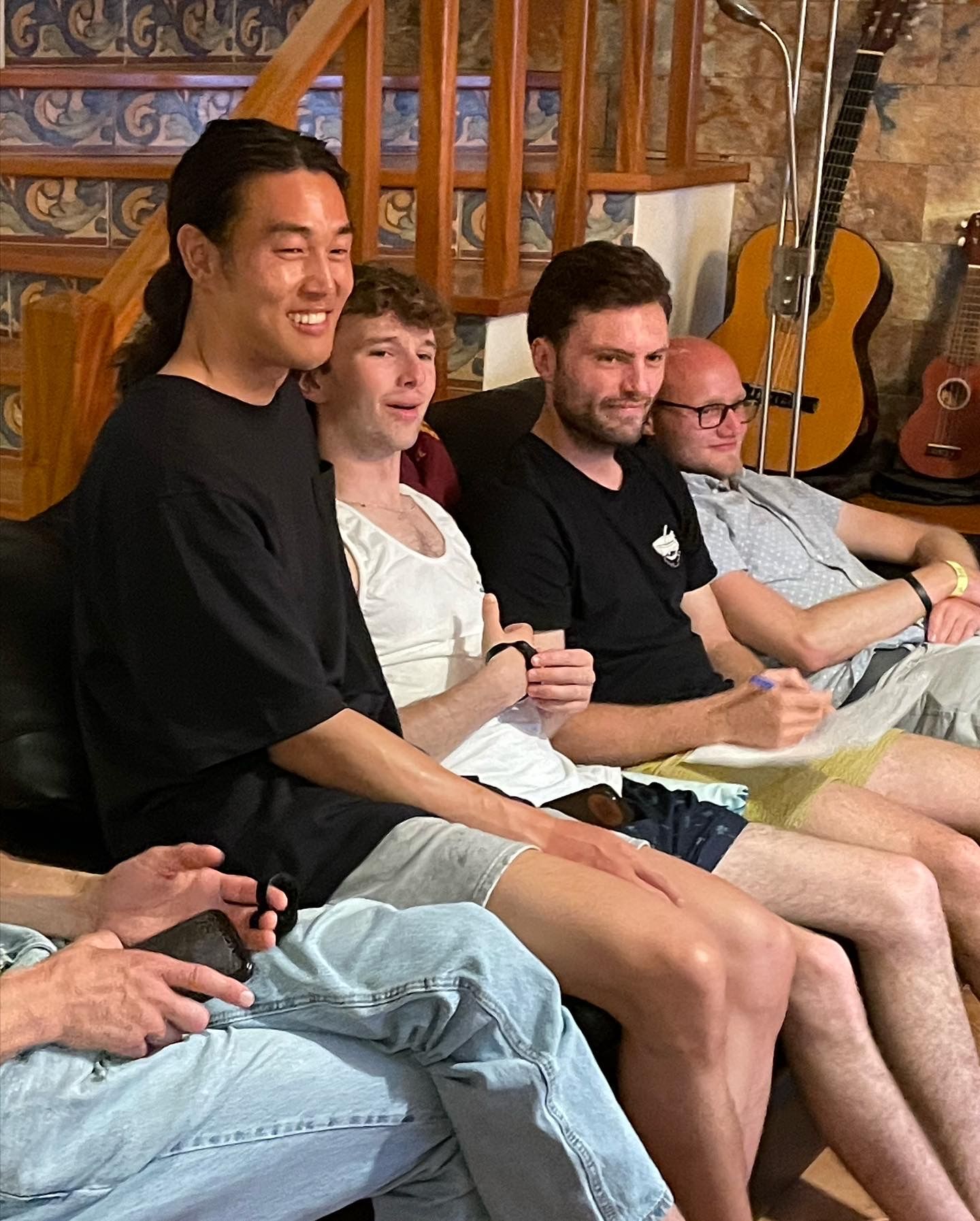 A group of men are sitting on a couch with guitars in the background.