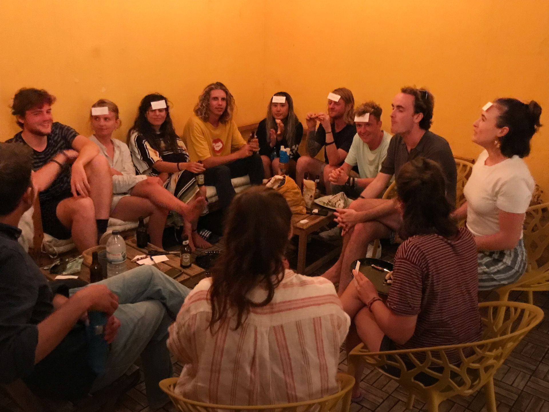 A group of people are sitting in a circle with cards on their heads