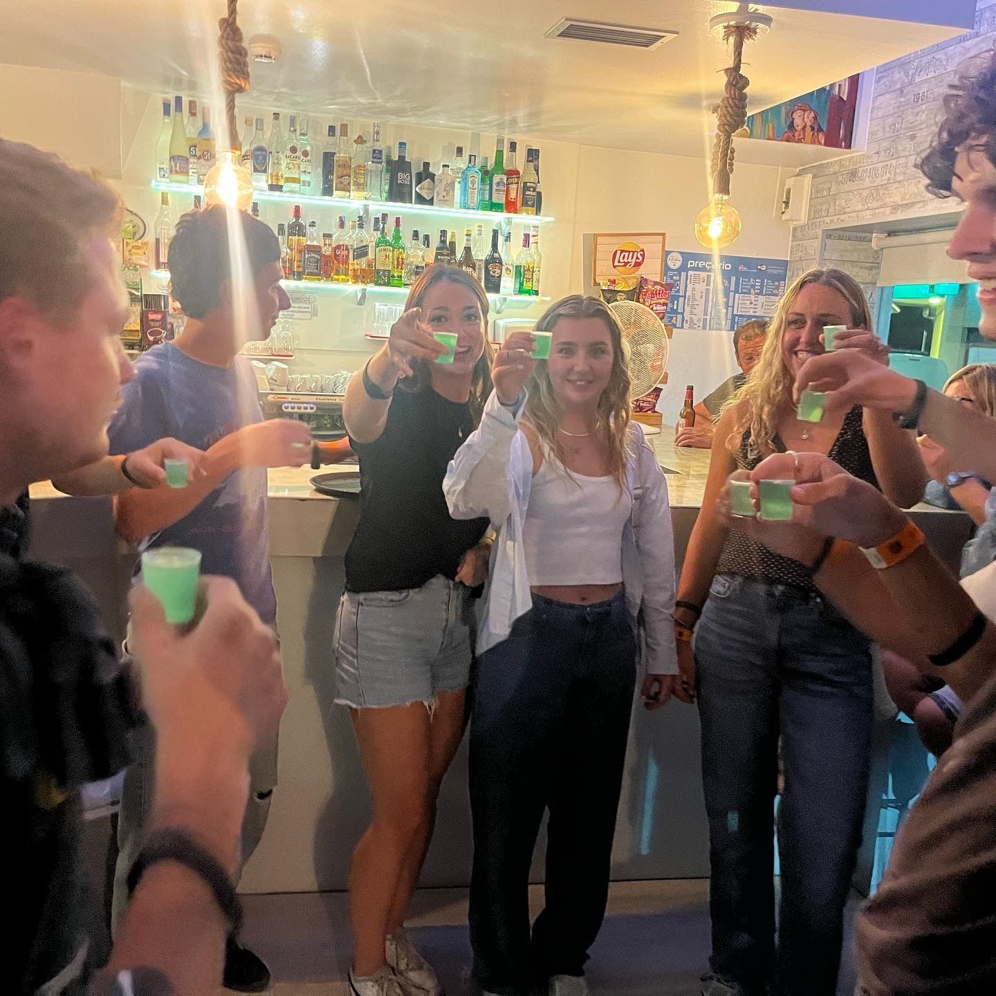 A group of people are standing around a bar holding shot glasses.