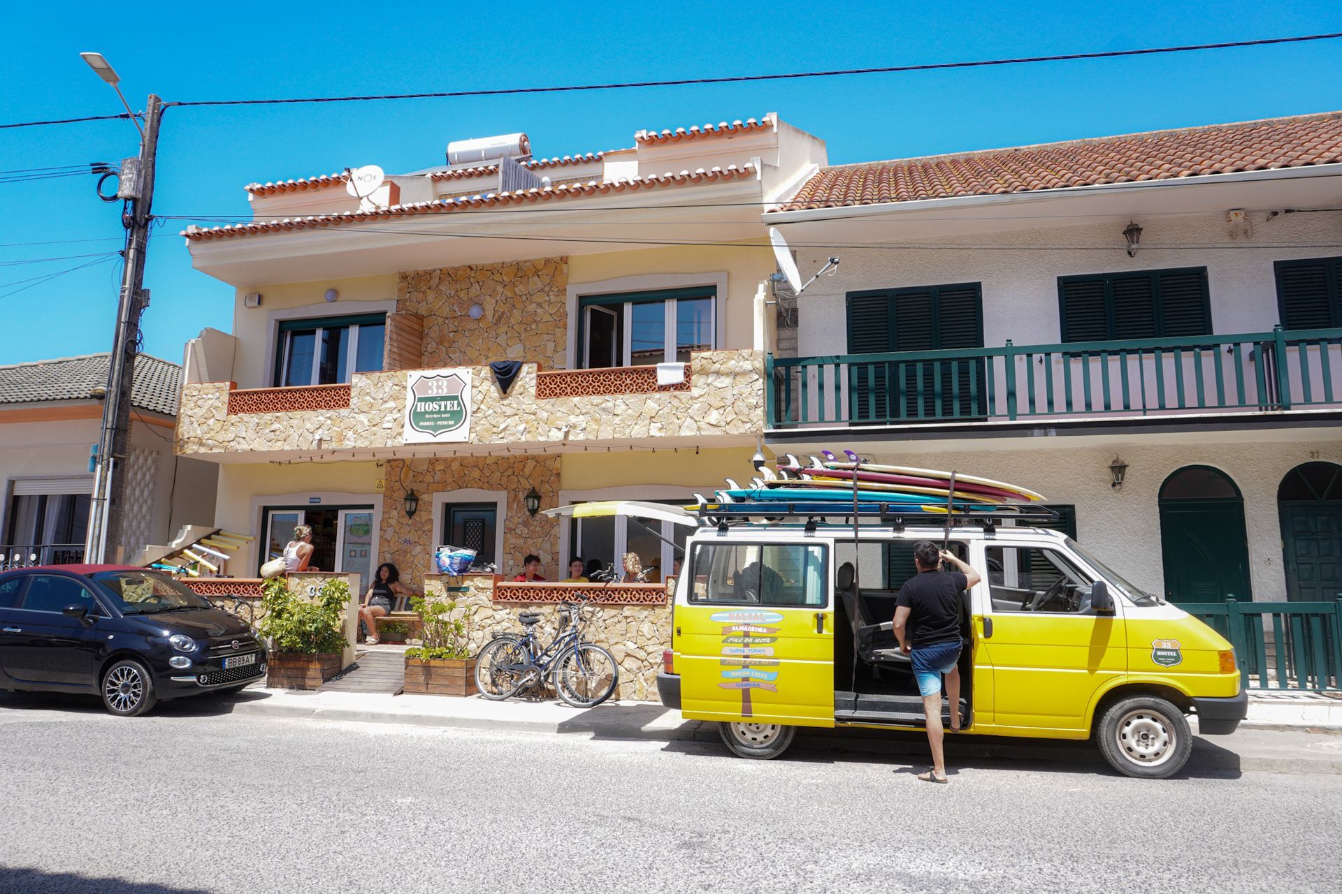 A yellow van with surfboards on top of it is parked in front of a building.