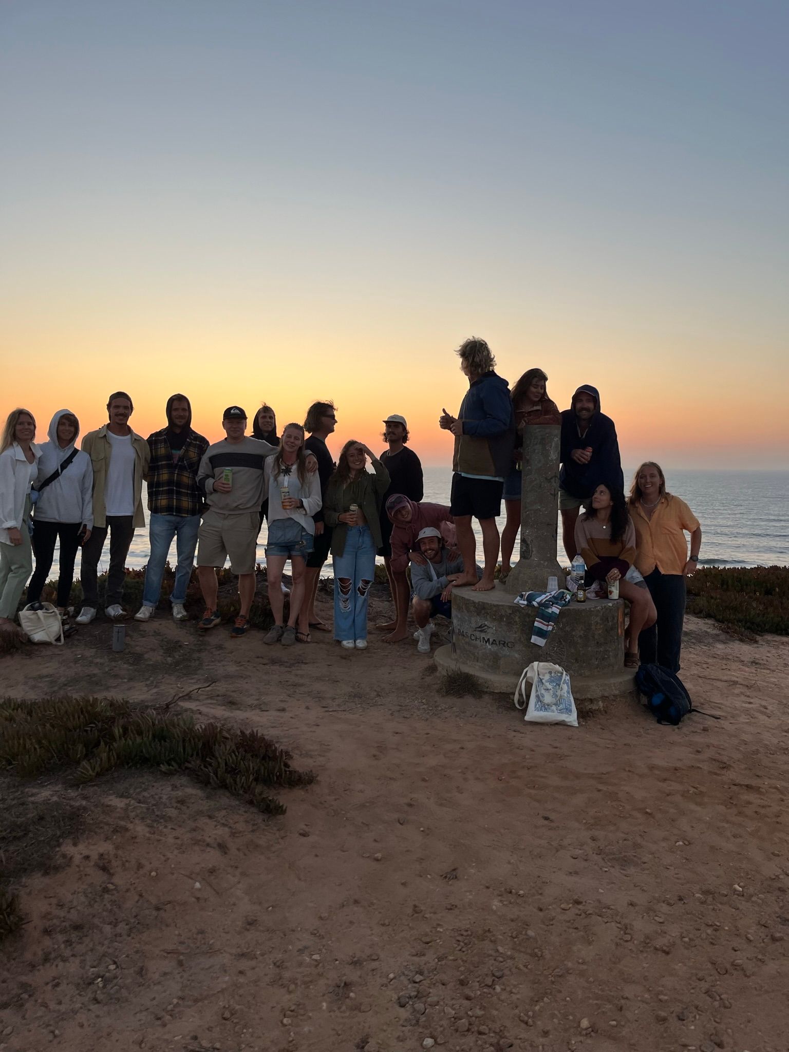 A group of people are posing for a picture on a beach at sunset.