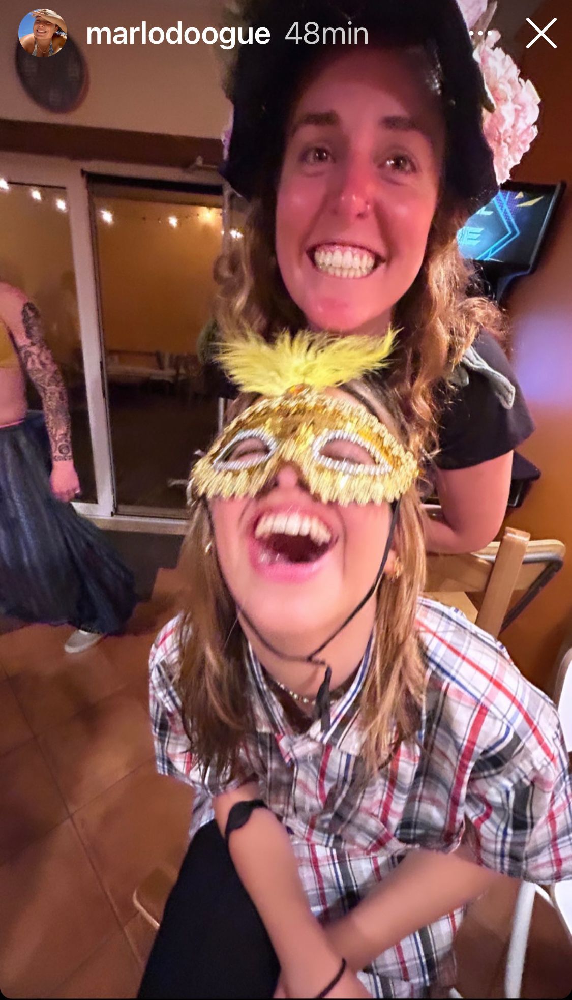 Two women wearing masks are laughing together in a room.
