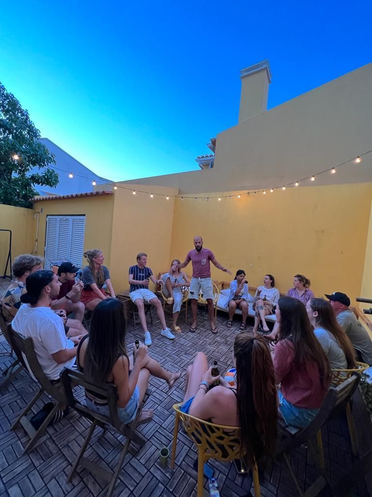 A group of people are sitting in a circle in front of a yellow building.