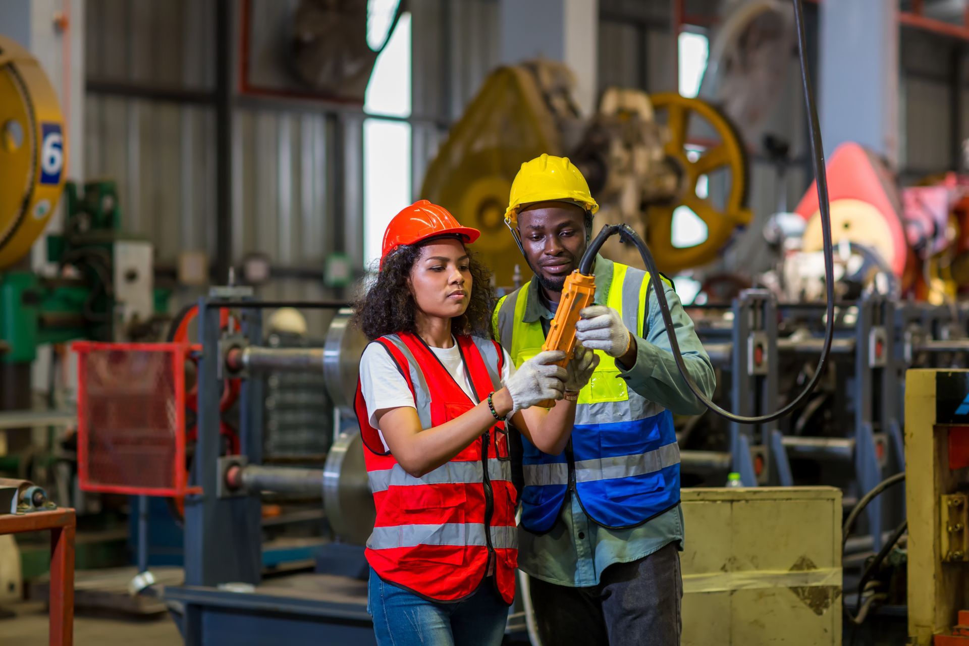 Two workers in safety vests and hard hats examining equipment in a factory.