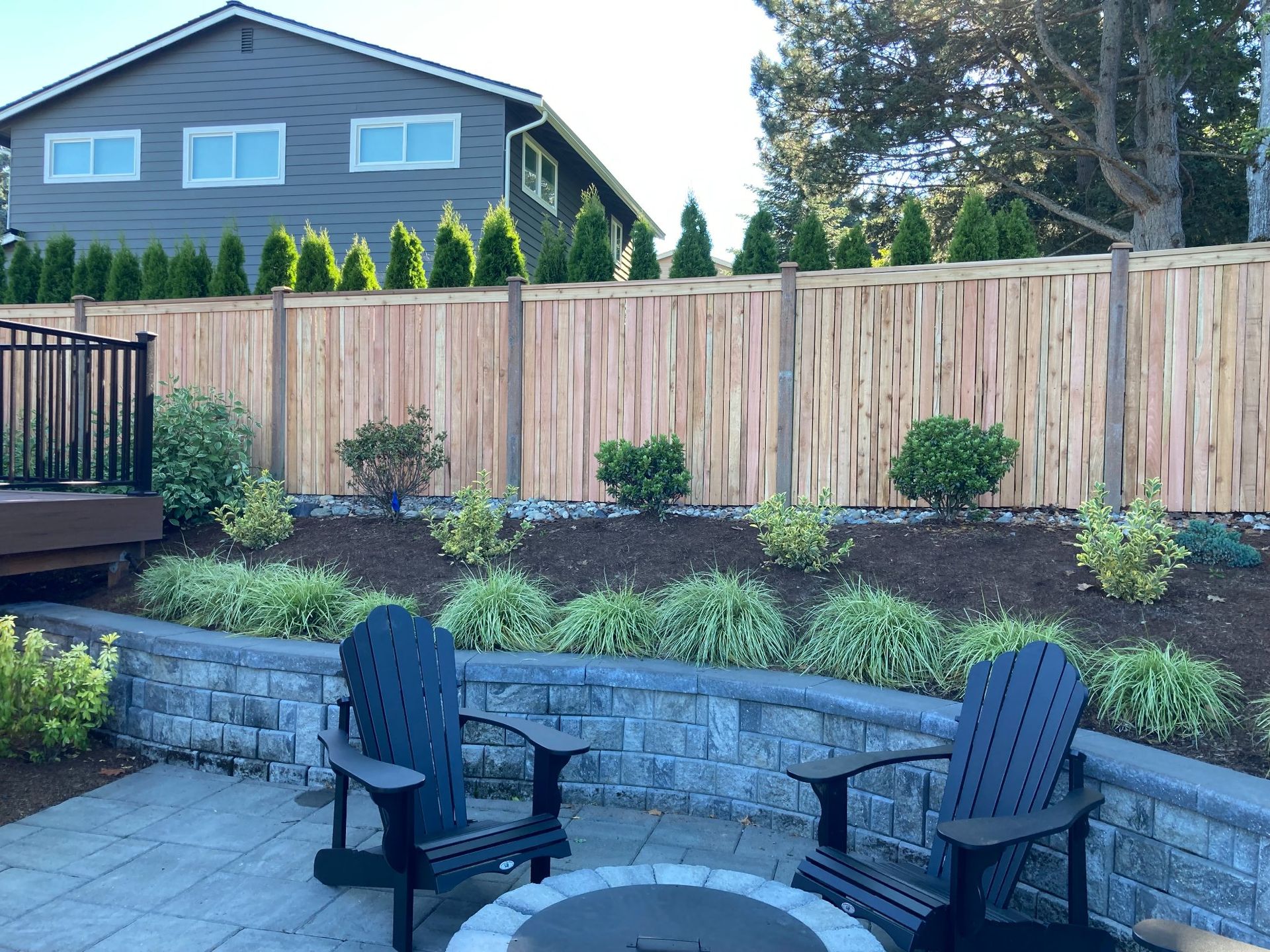 Patio with Adirondack chairs, low stone wall, and wooden fence with landscaping.