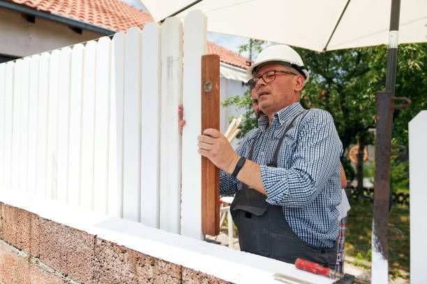 A senior contractor using a level to measure white wooden timber, as part of fence repair services.