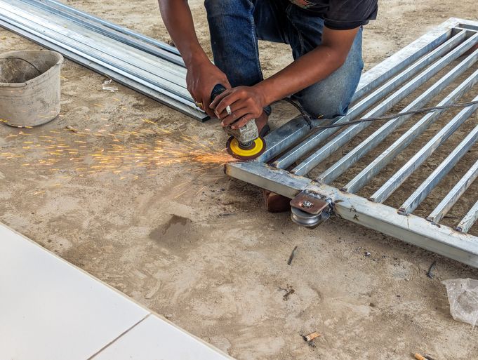 A fence worker is smoothing an iron fence using a grinding machine A fence worker is smoothing an iron fence using a grinding machine