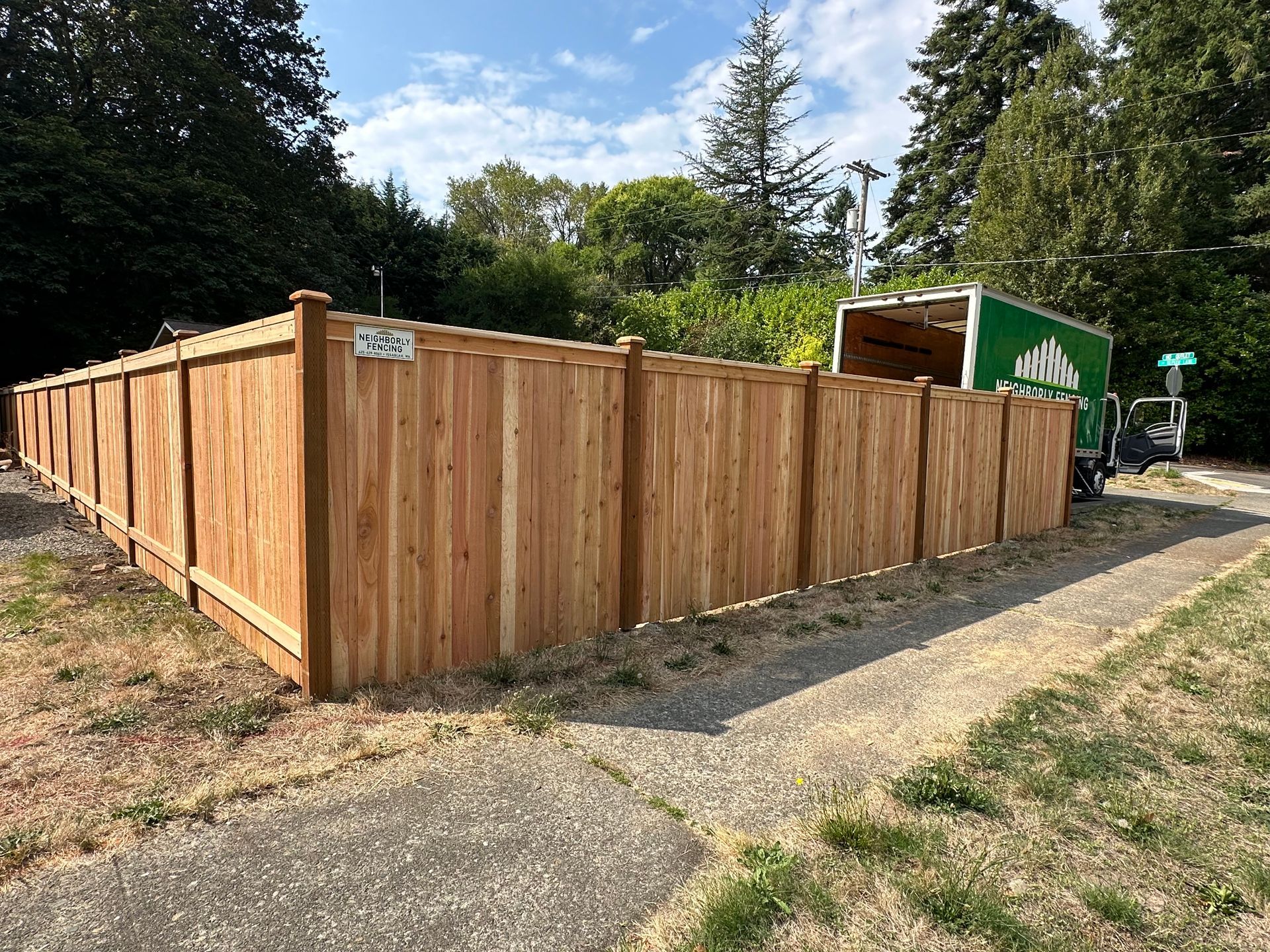 Wooden fence alongside a sidewalk, with a green truck in the background. Wooden fence alongside a sidewalk, with a green truck in the background.