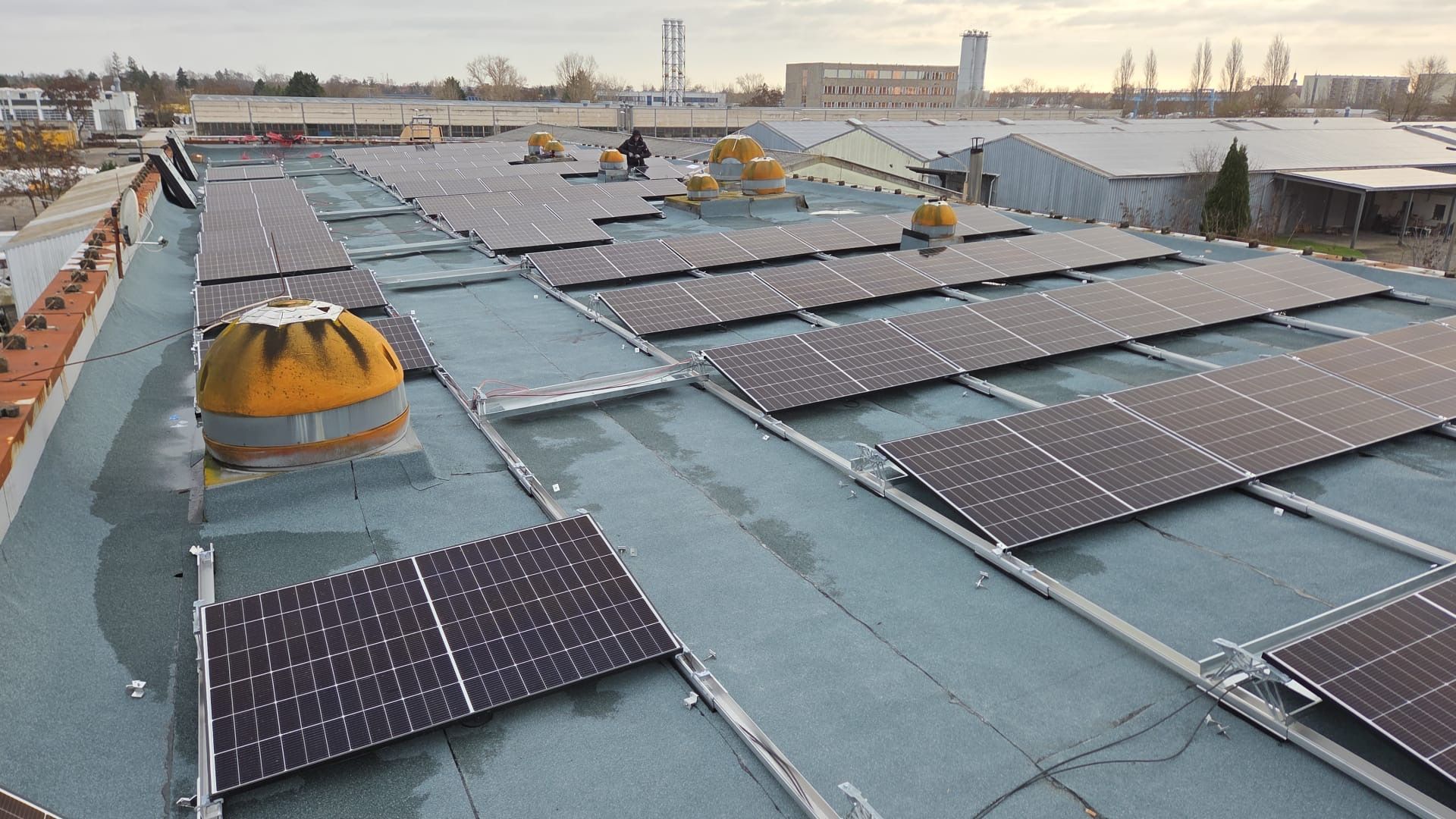 Rooftop covered with solar panels and skylights at sunset, with city buildings in the distance