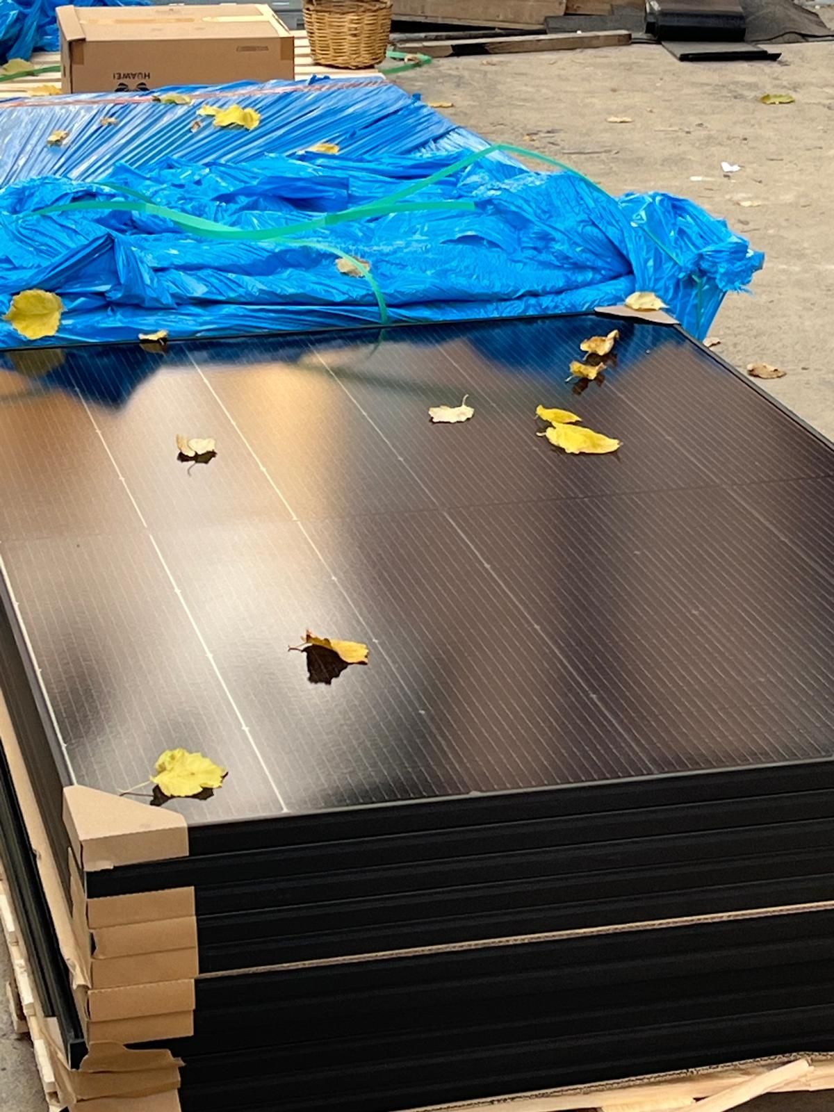 Stacked black carbon fiber sheets covered partly by a blue tarp in an outdoor storage area