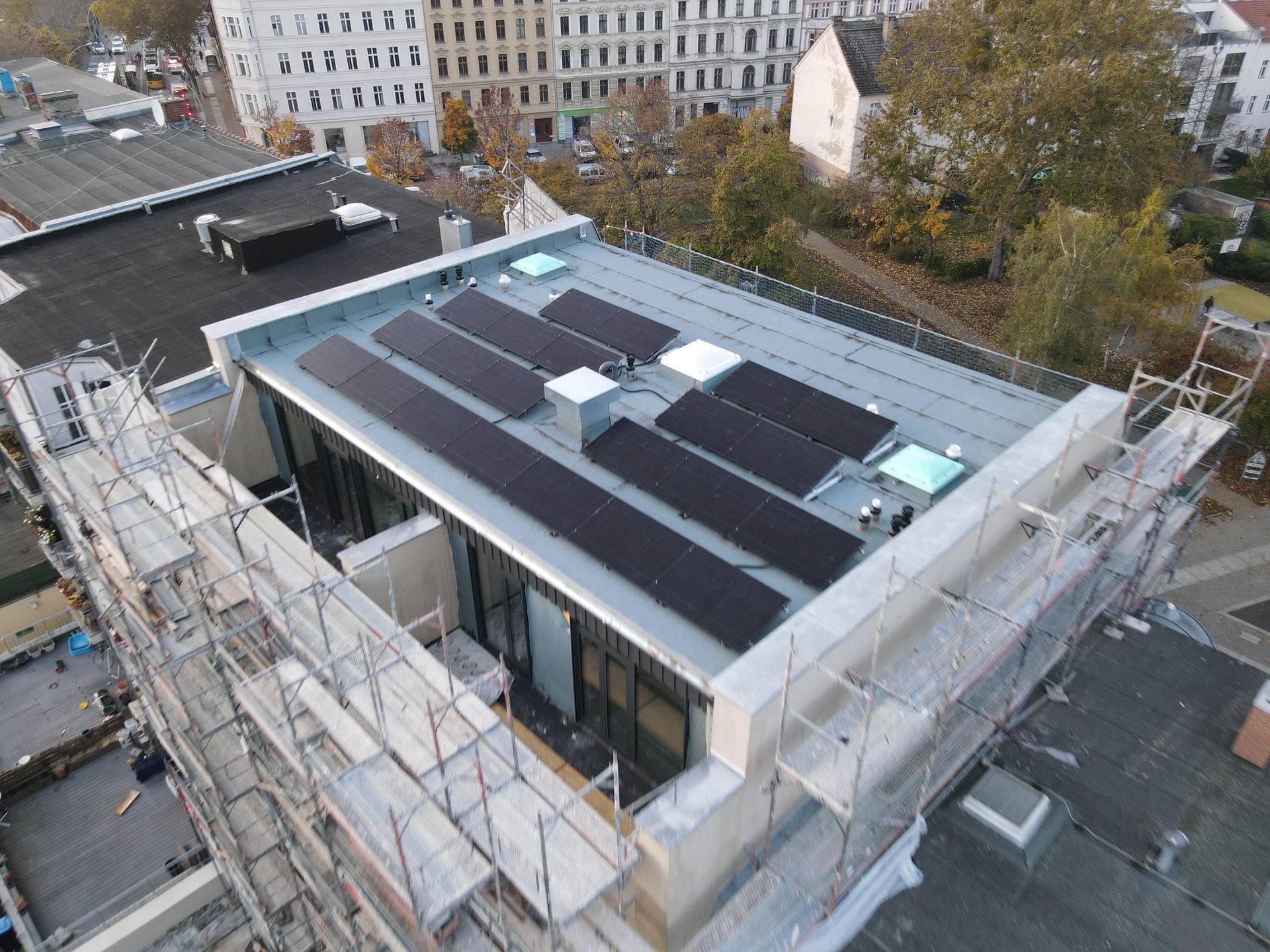 Aerial view of a flat-roof building under construction with scaffolding and neighboring buildings nearby