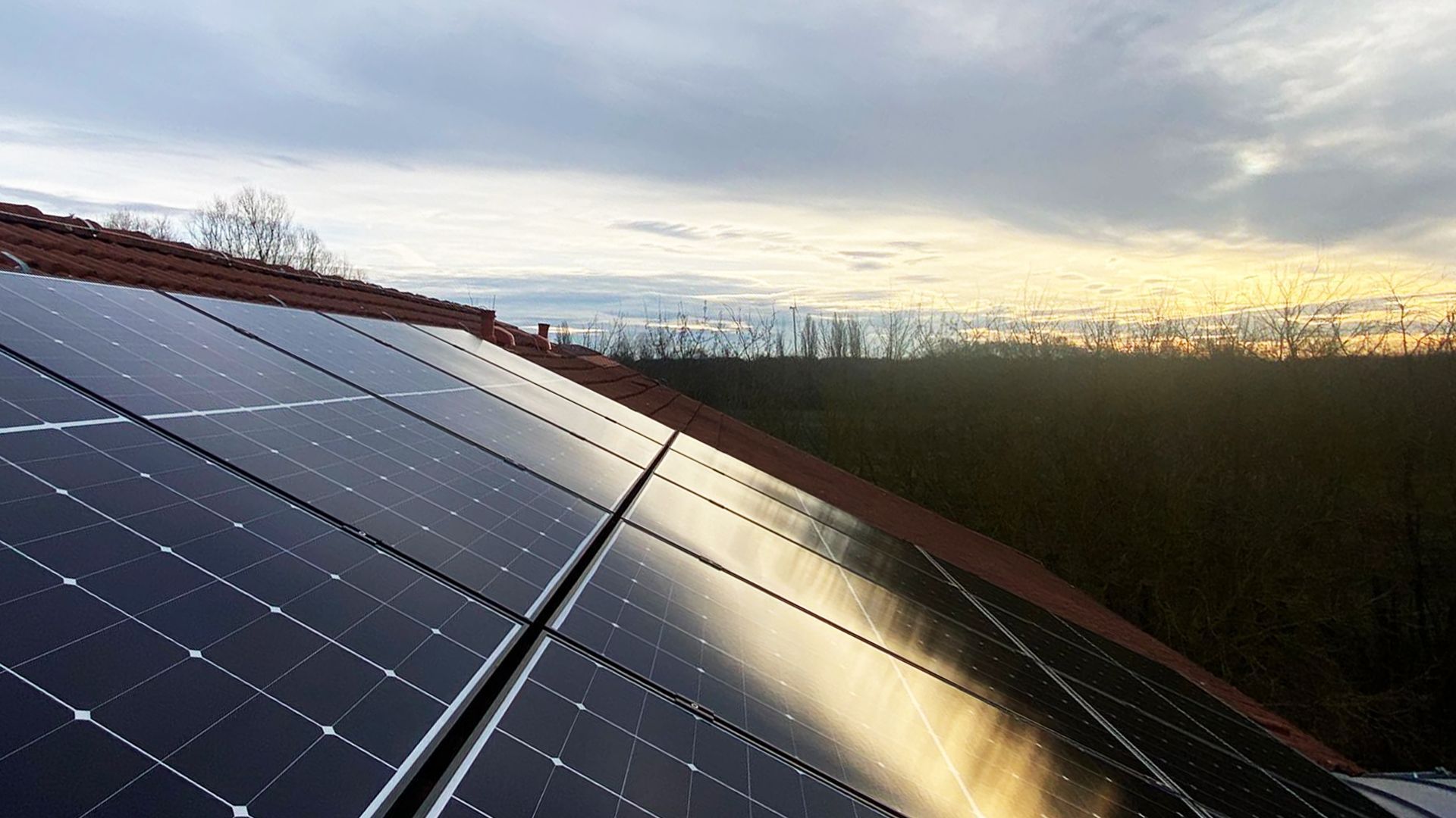 Solar panels on a roof at sunset with cloudy sky reflecting on the panels.