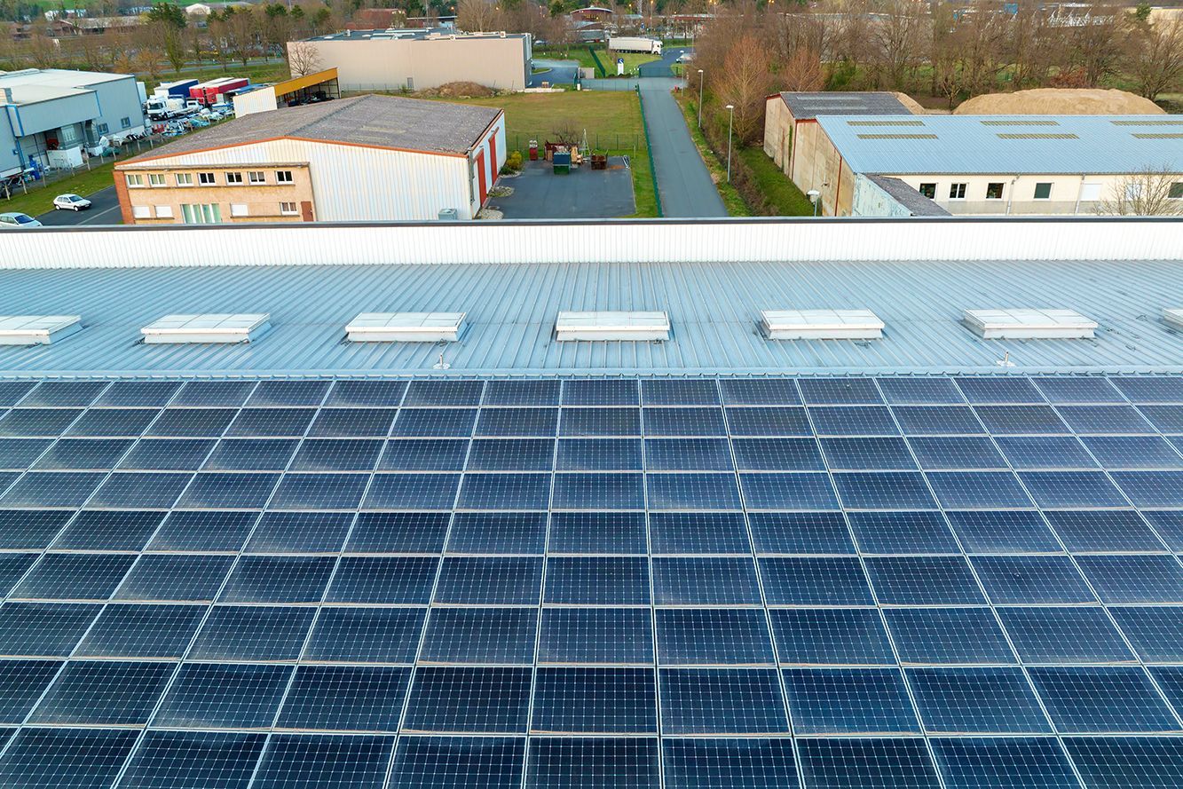 Solar panels covering a rooftop with industrial buildings and trees in the background