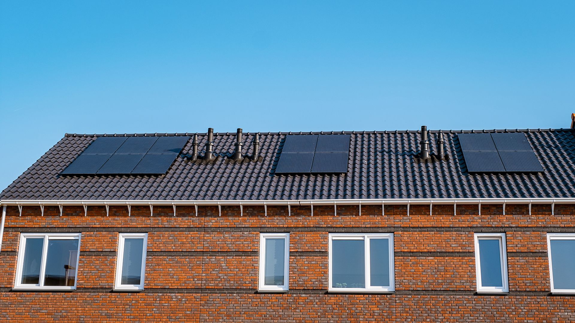 Red brick apartment roof with solar panels under a clear blue sky