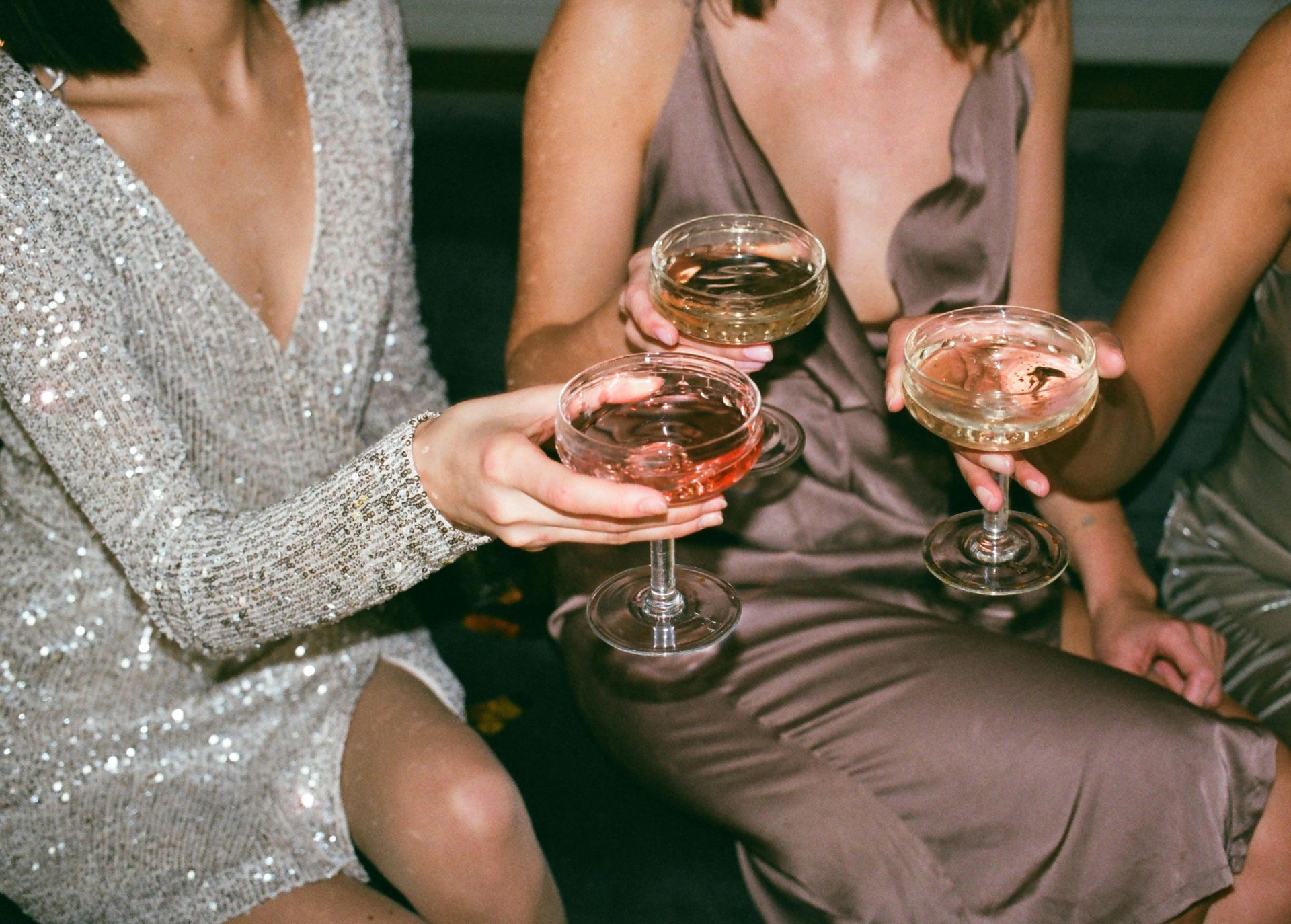 Three women in party dresses clink champagne glasses.