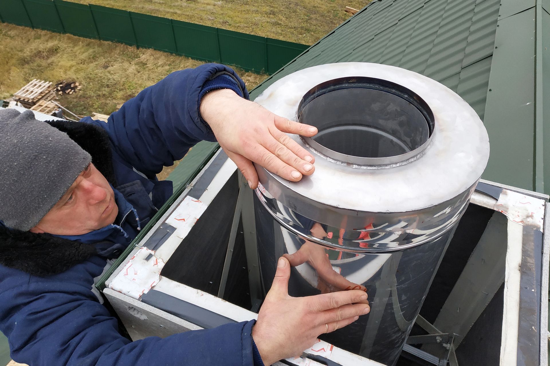 Persona che installa con entrambe le mani una lucida griglia di ventilazione per camino su un tetto
