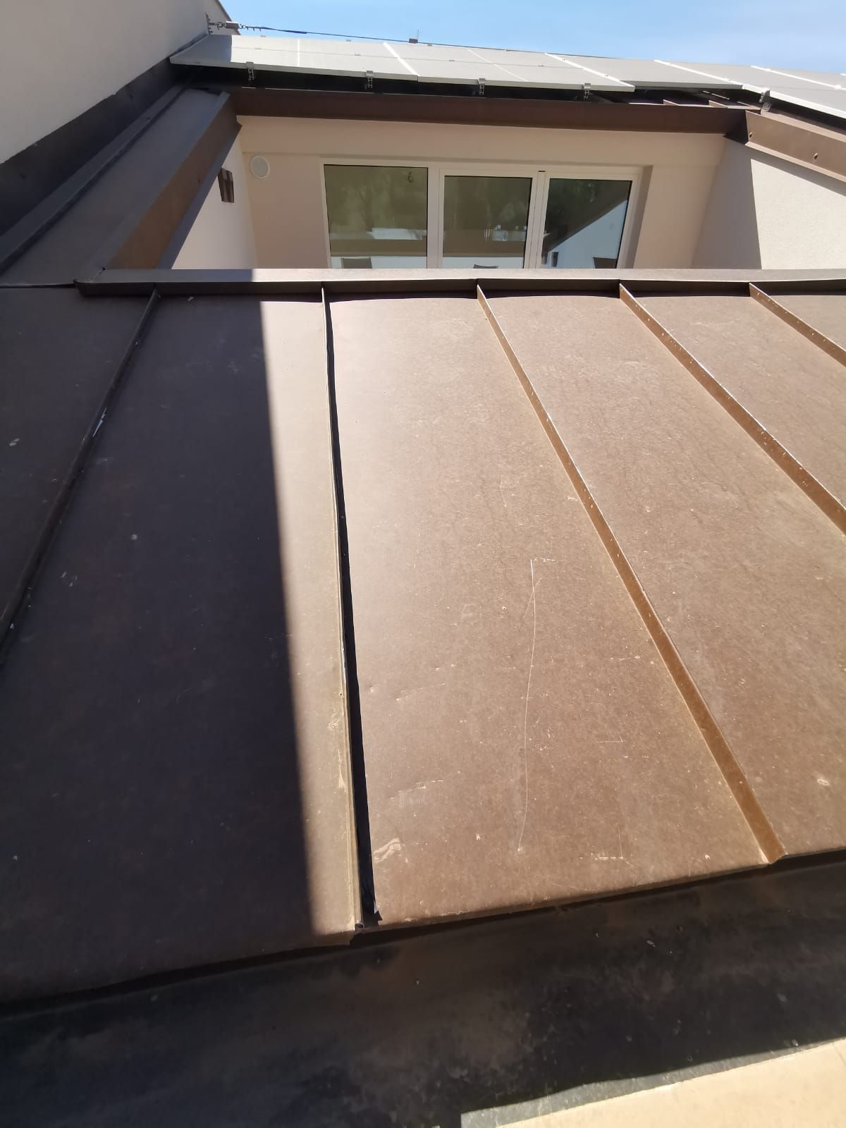 Tetto e abbaino con pannelli metallici marroni e finiture scure sotto un cielo nuvoloso.