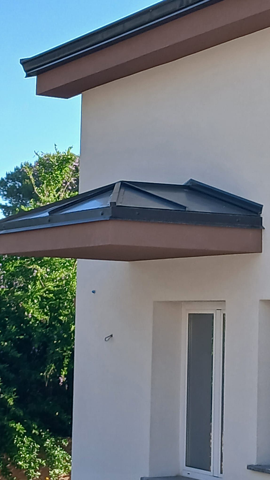 Esterno di una moderna casa bianca con tetto scuro e aggetti angolari, sullo sfondo di un cielo blu.