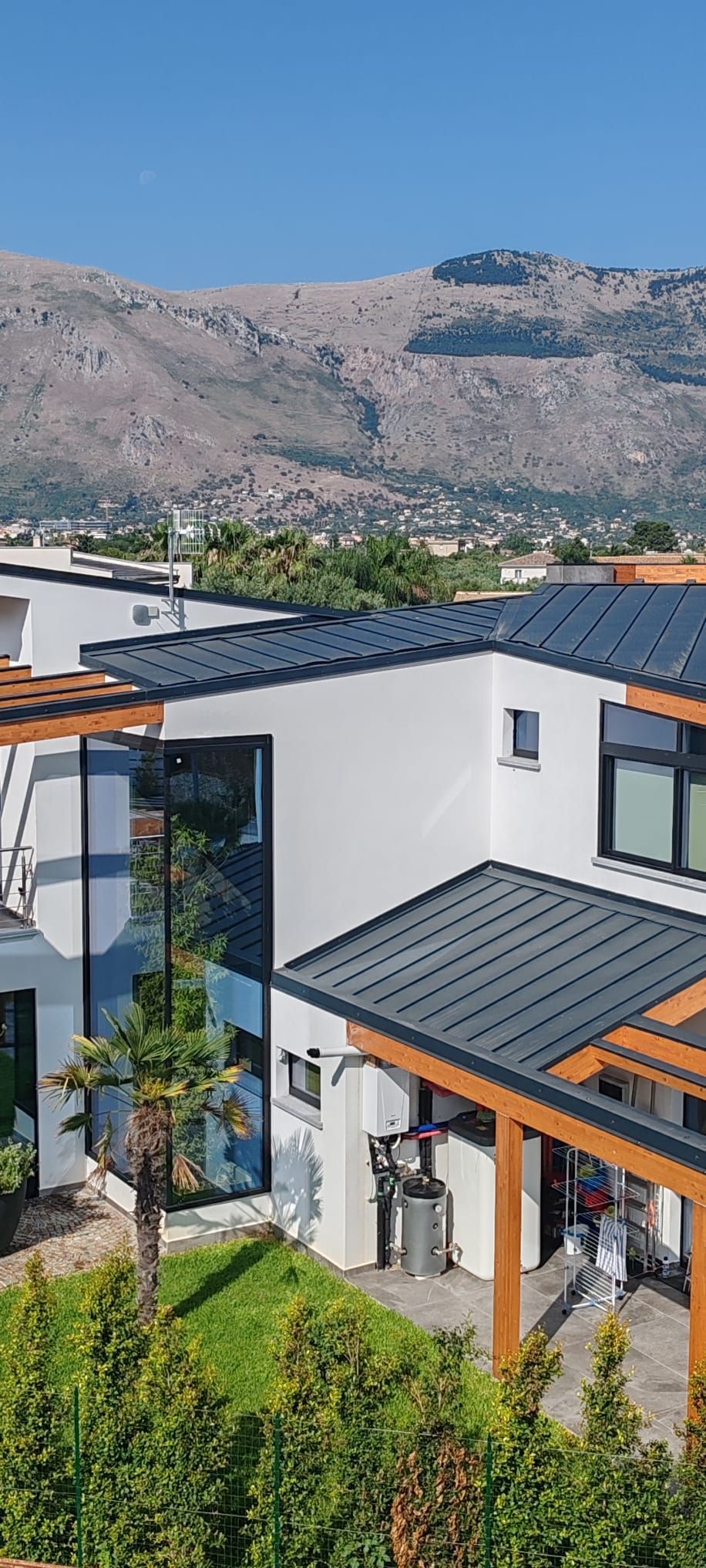 Casa moderna bianca con tetto scuro e dettagli arancioni, sullo sfondo delle montagne sotto un cielo limpido.