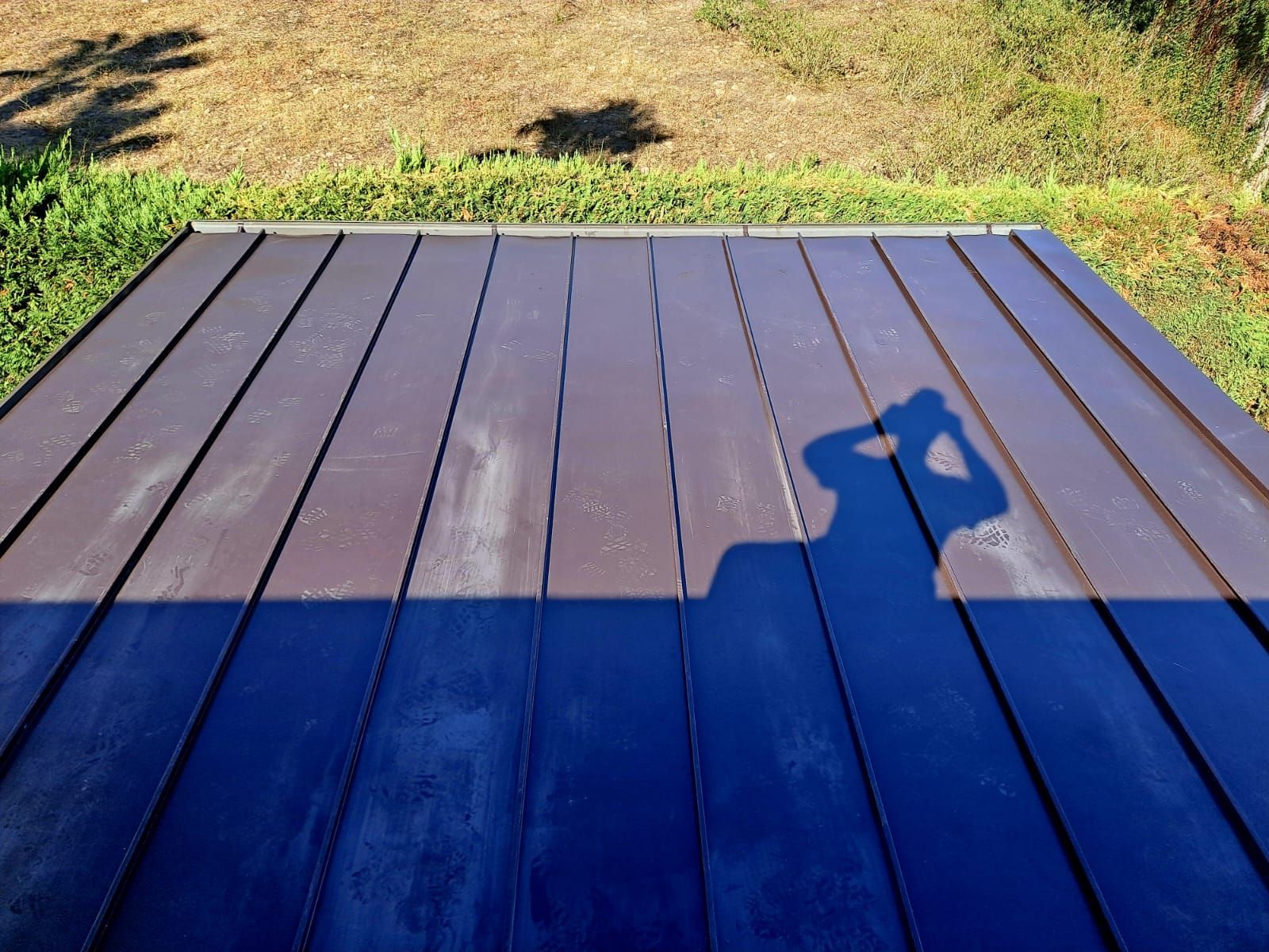 Terrazza in legno dipinta di blu in un giardino soleggiato, con l'ombra di una persona che tiene in mano una macchina fotografica.