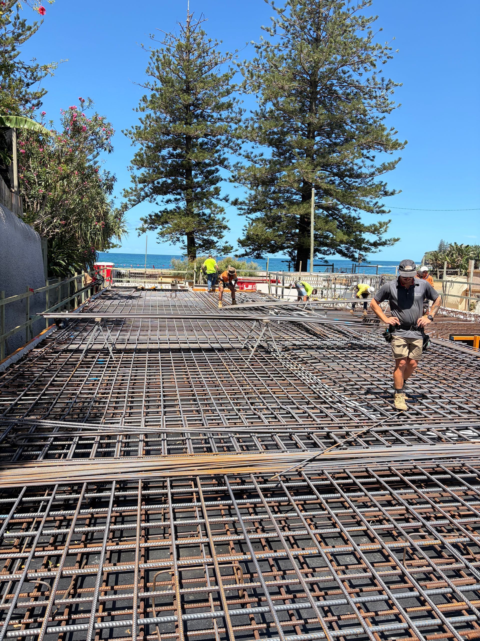 Construction workers on a site with rebar. The ocean is in the background, blue sky, sunny day.