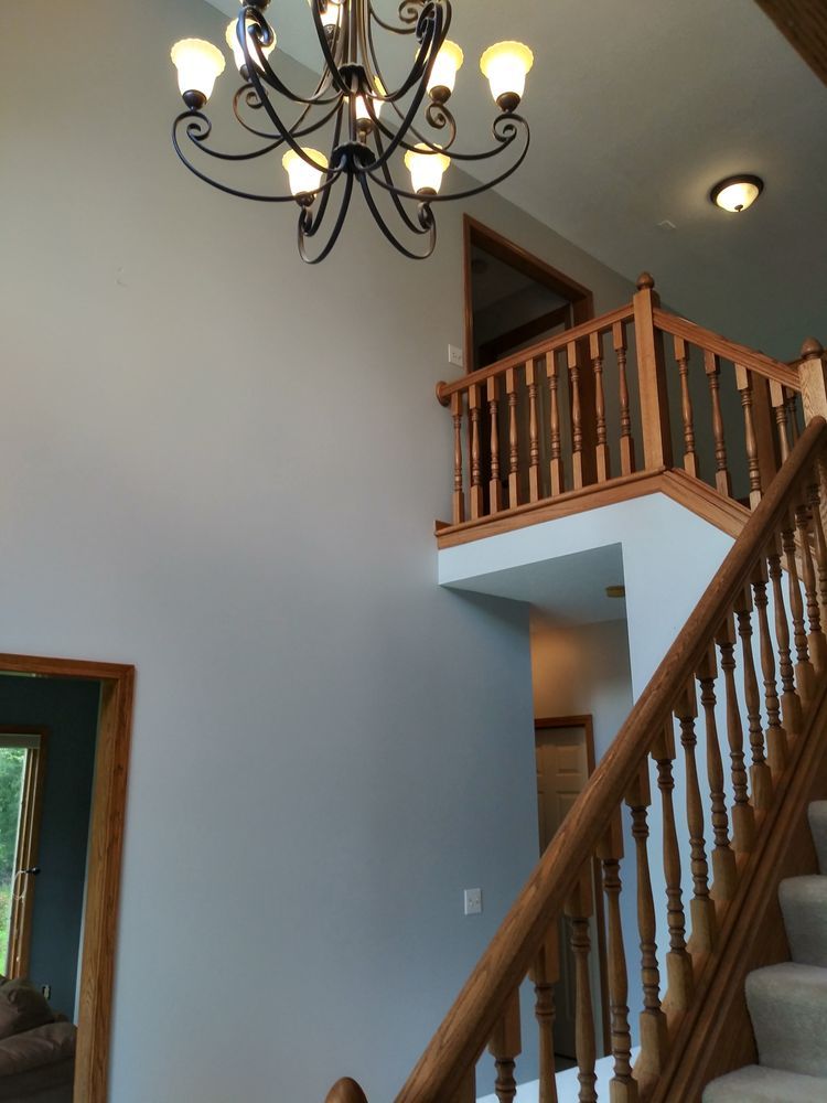 A foyer with a staircase and chandelier. Wooden banisters, gray walls, and a light fixture.