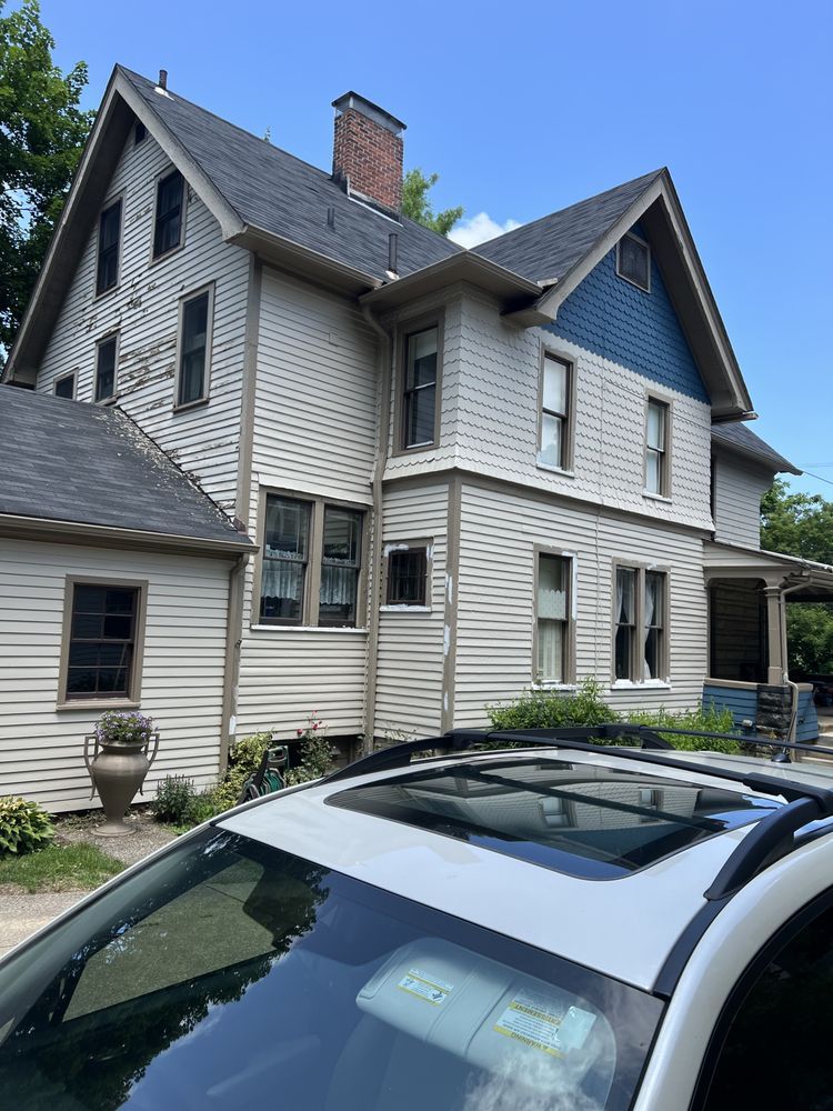 Side view of a light-colored two-story house with a dark roof, blue gable, and car in front.