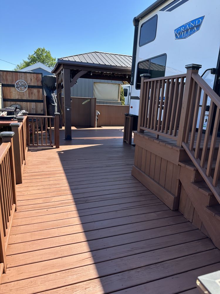 Wooden deck with brown railing. RV parked to the right. Gazebo in the background.