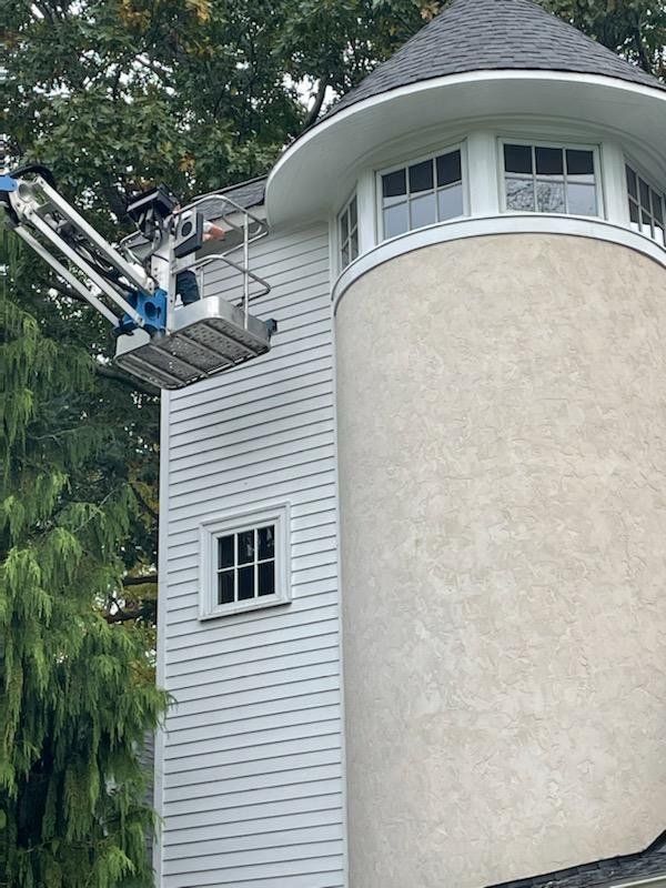 A white tower being worked on from a mechanical lift, trees in the background.