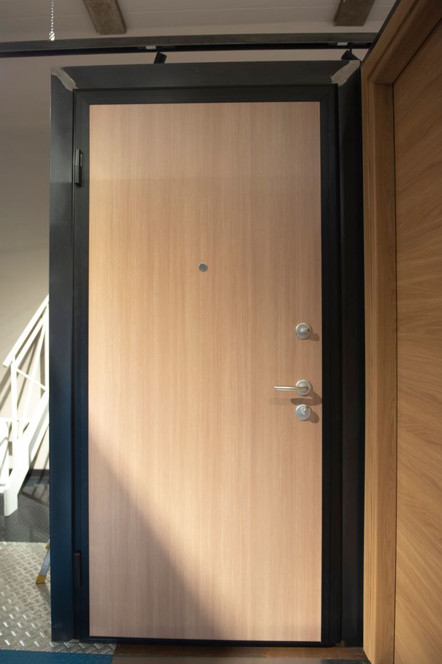 Porta di legno con cornice nera, spioncino e maniglia argentata. Luce del sole sulla destra.