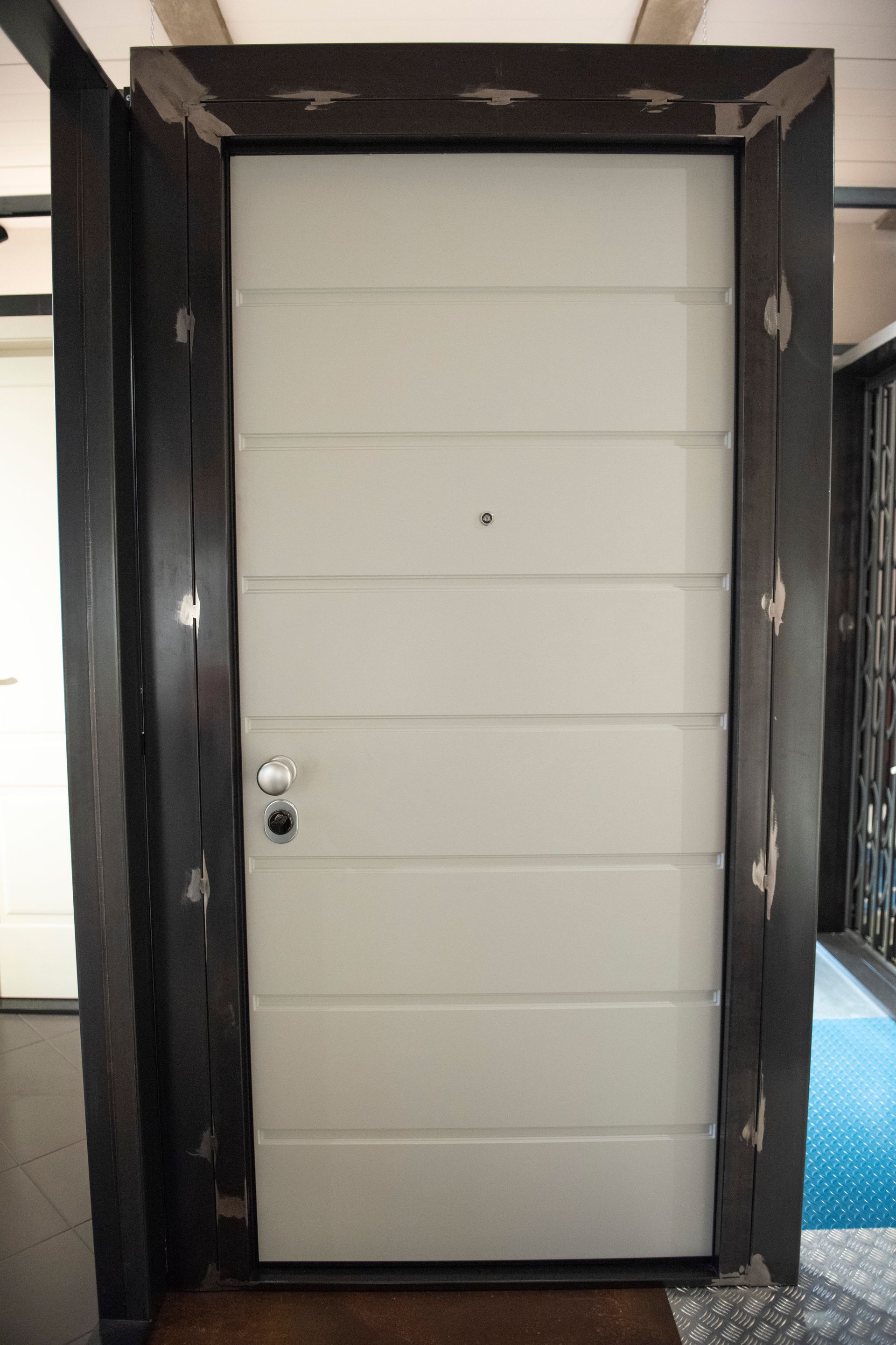 Una porta chiusa grigio chiaro con pannelli orizzontali, inserita in una cornice marrone scuro con dettagli decorativi in ​​metallo.